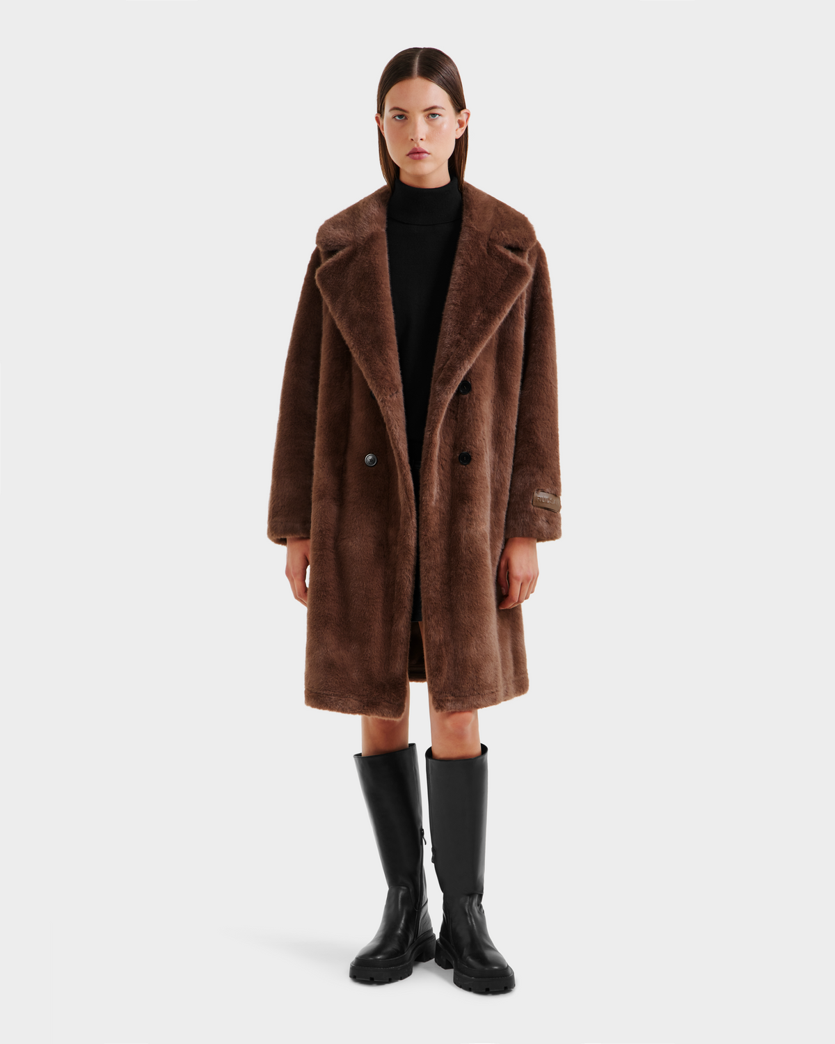 A woman faces forward, wearing the Rudsak SIENA - 8125542 Mocha faux fur coat over a black outfit and knee-high black boots, against a plain white background.