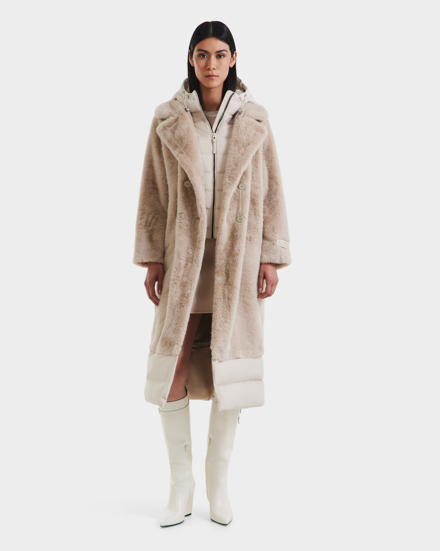 A woman stands facing forward against a plain white background, wearing the Rudsak SIENA - 8125542 Vanilla faux fur coat over a light down coat, paired with a short skirt and white knee-high boots.