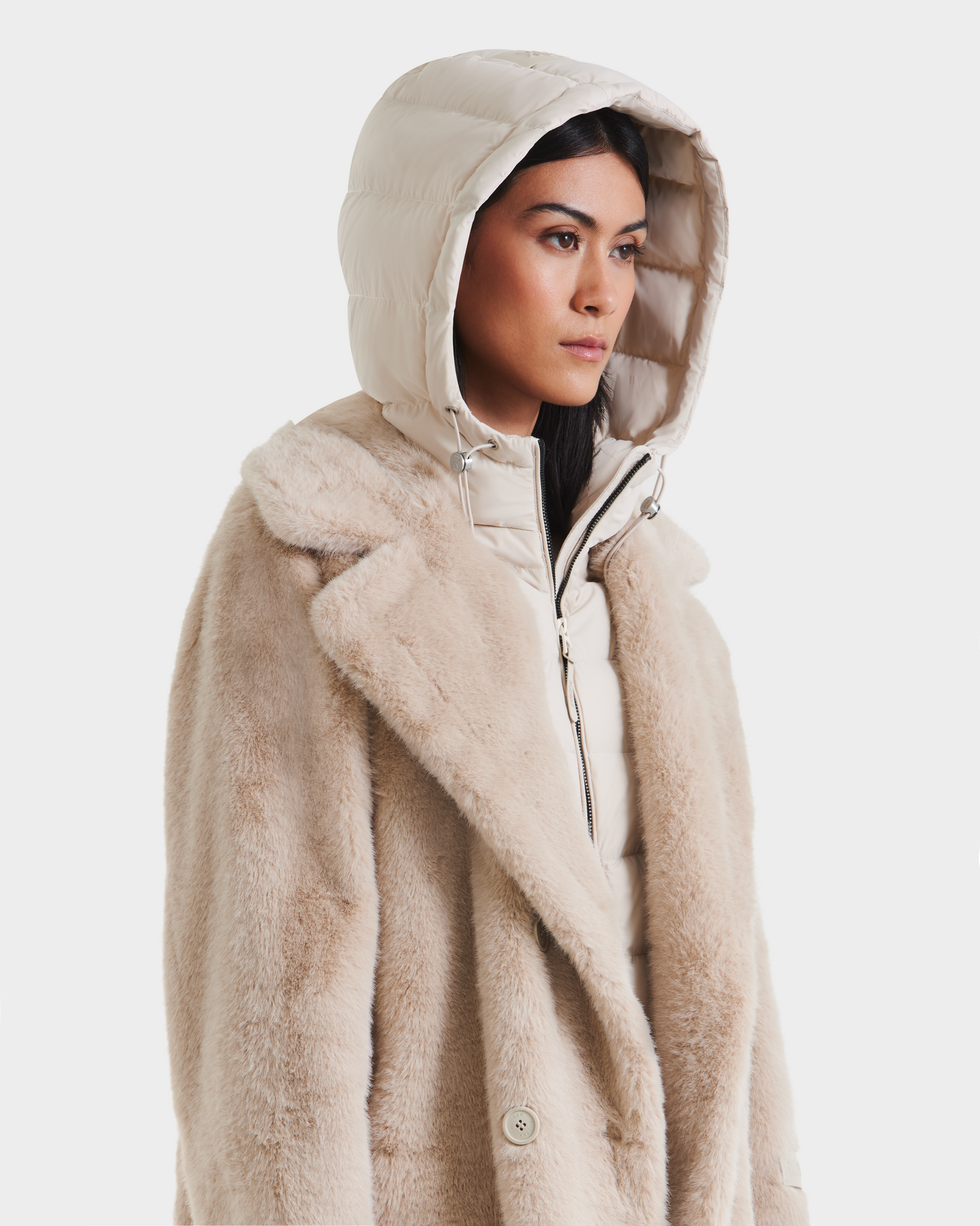 A woman models the Rudsak SIENA - 8125542 Vanilla faux fur coat over a quilted hooded jacket, looking to the side against a plain white background.