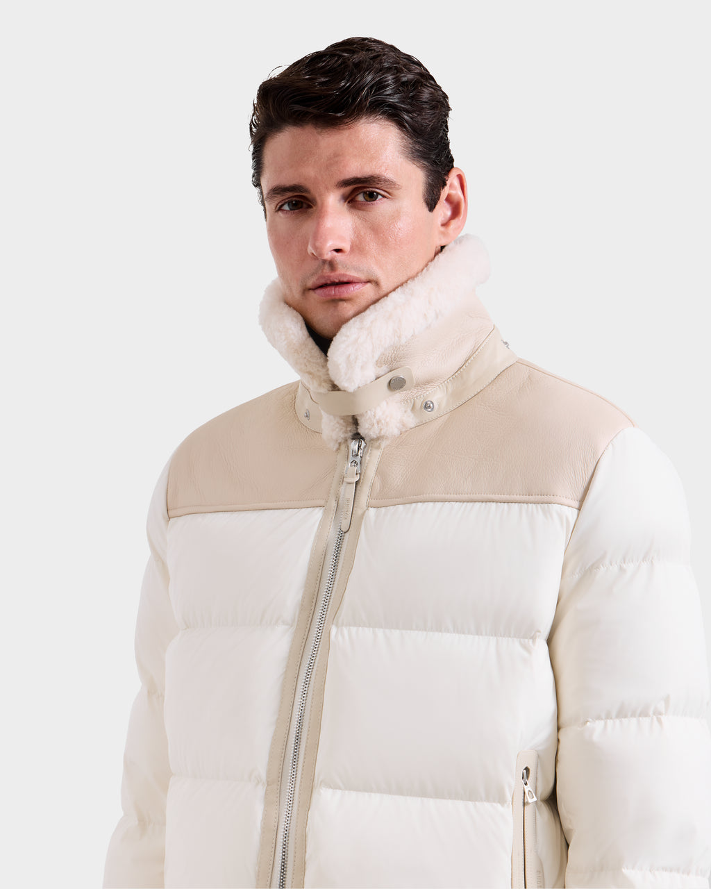 A man wears the Rudsak SIMON - 6125597 Vanilla men's quilted down puffer with a beige collar and shoulder detail, plus shearling lining around the neck, looking slightly to the side against a plain background.