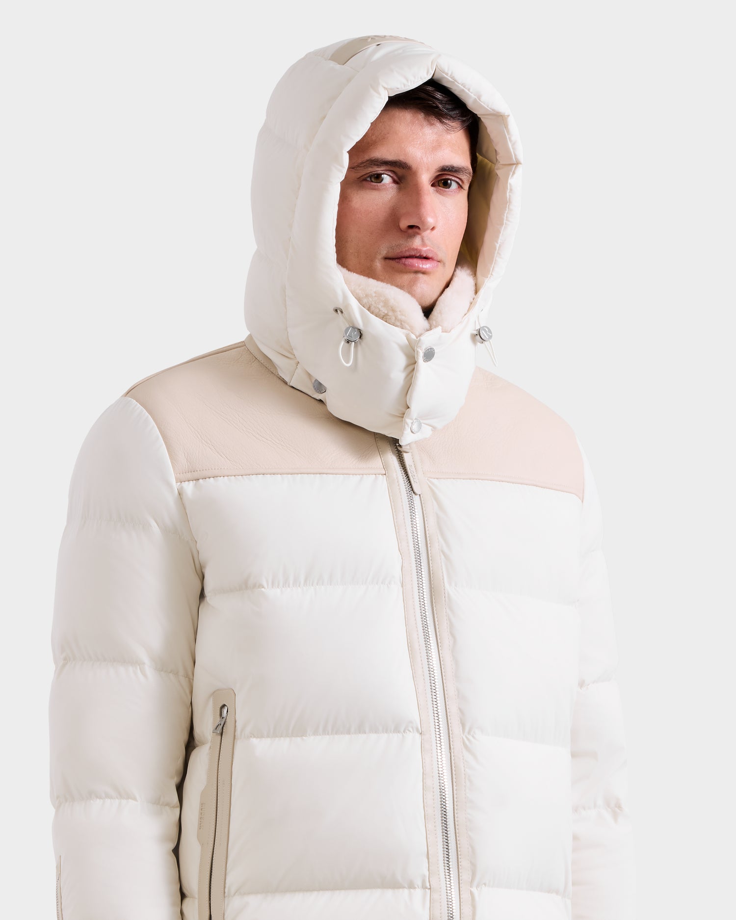 A man wears the Rudsak SIMON - 6125597 Vanilla men’s quilted down puffer jacket with a high collar, standing against a plain white background.