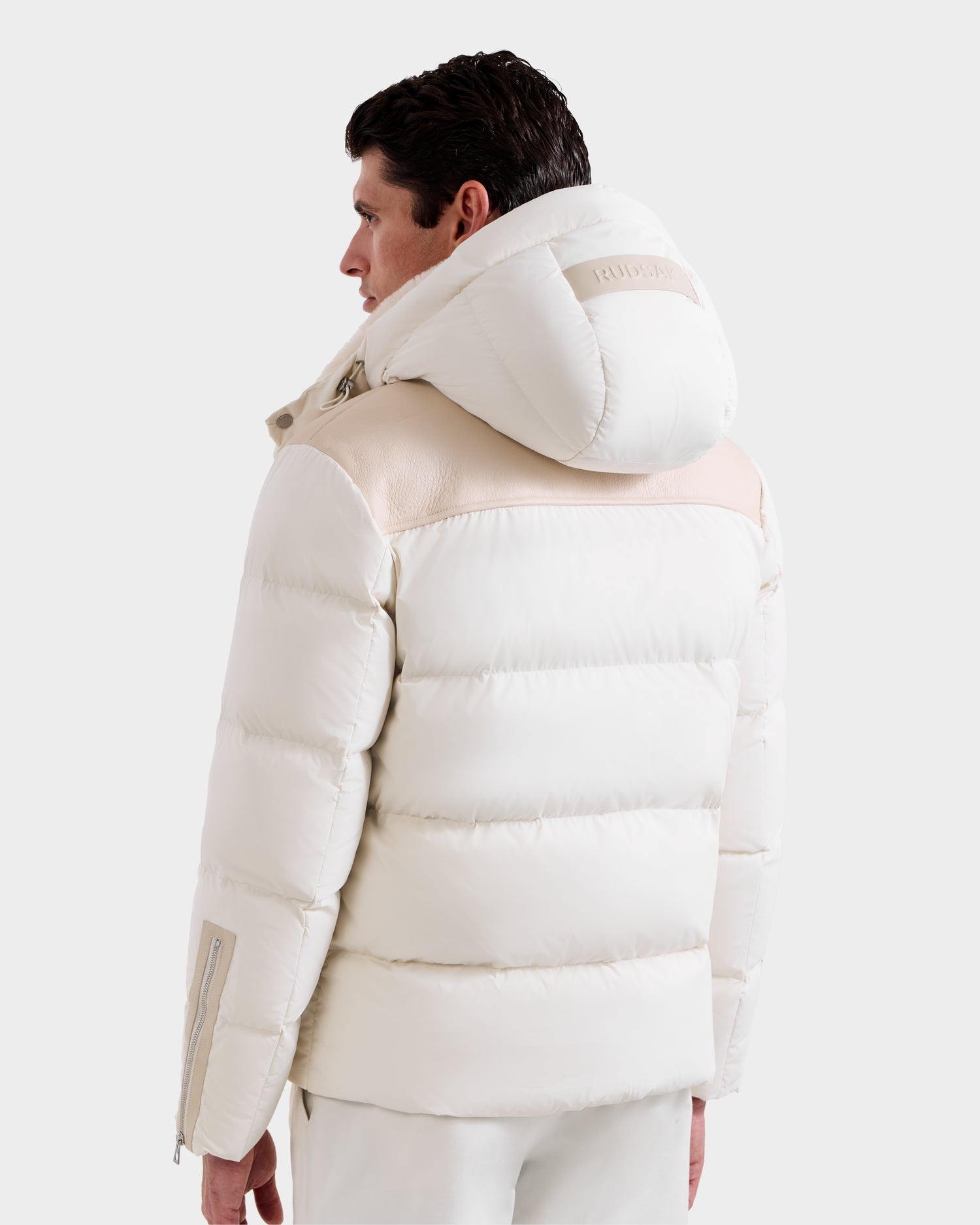 A person wearing the Rudsak SIMON - 6125597 Vanilla men’s quilted down puffer with a large hood and beige shoulder detail, viewed from the back against a plain light background.