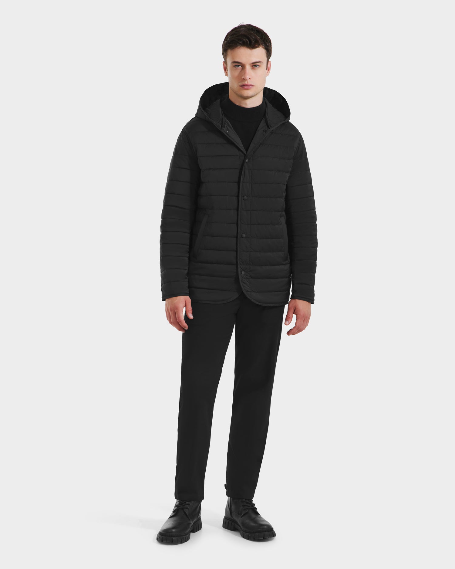 A man faces forward against a plain white background, wearing the Rudsak STANTON - 6125531 Black technical shell overcoat with a quilted inner puffer, paired with black shirt, pants, and shoes.