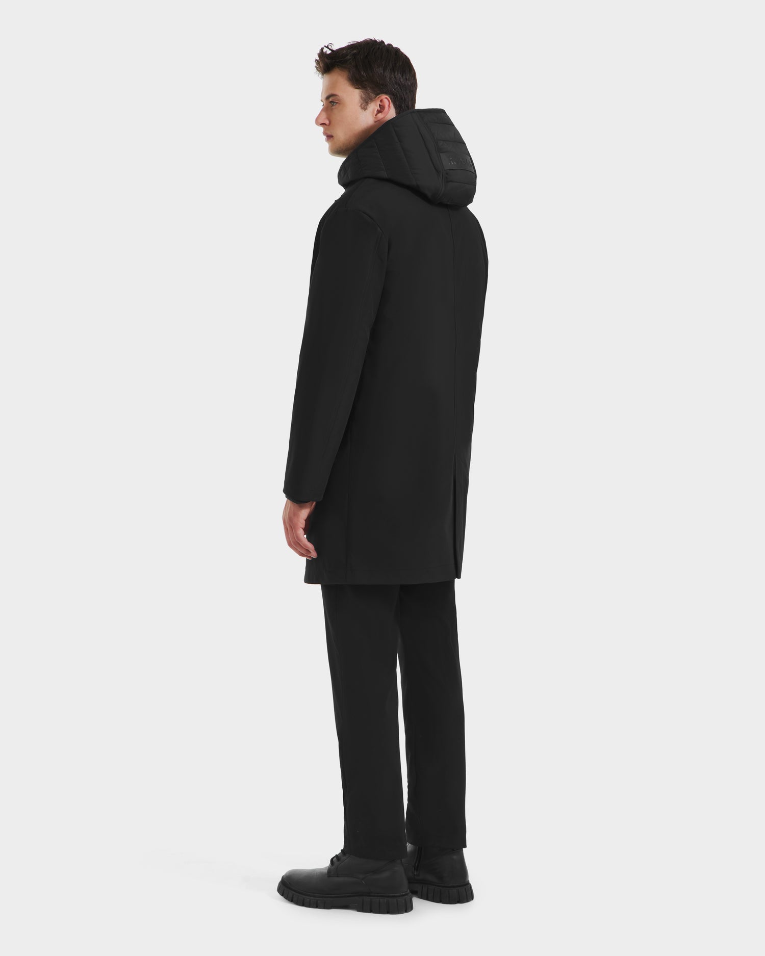A man in the Rudsak STANTON - 6125531 black 3-in-1 overcoat, with a technical shell and quilted inner puffer jacket, stands facing away and slightly to the side against a plain white background.
