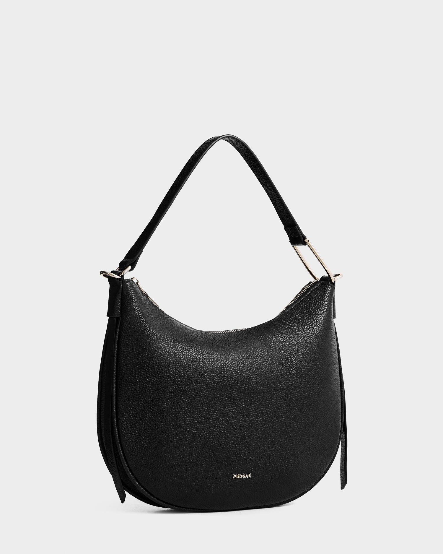The SYLVIA - L325515 Black by Rudsak is a women’s leather shoulder bag featuring a curved crescent silhouette, single strap, gold hardware, and a subtle brand logo near the bottom, shown against a plain light background.