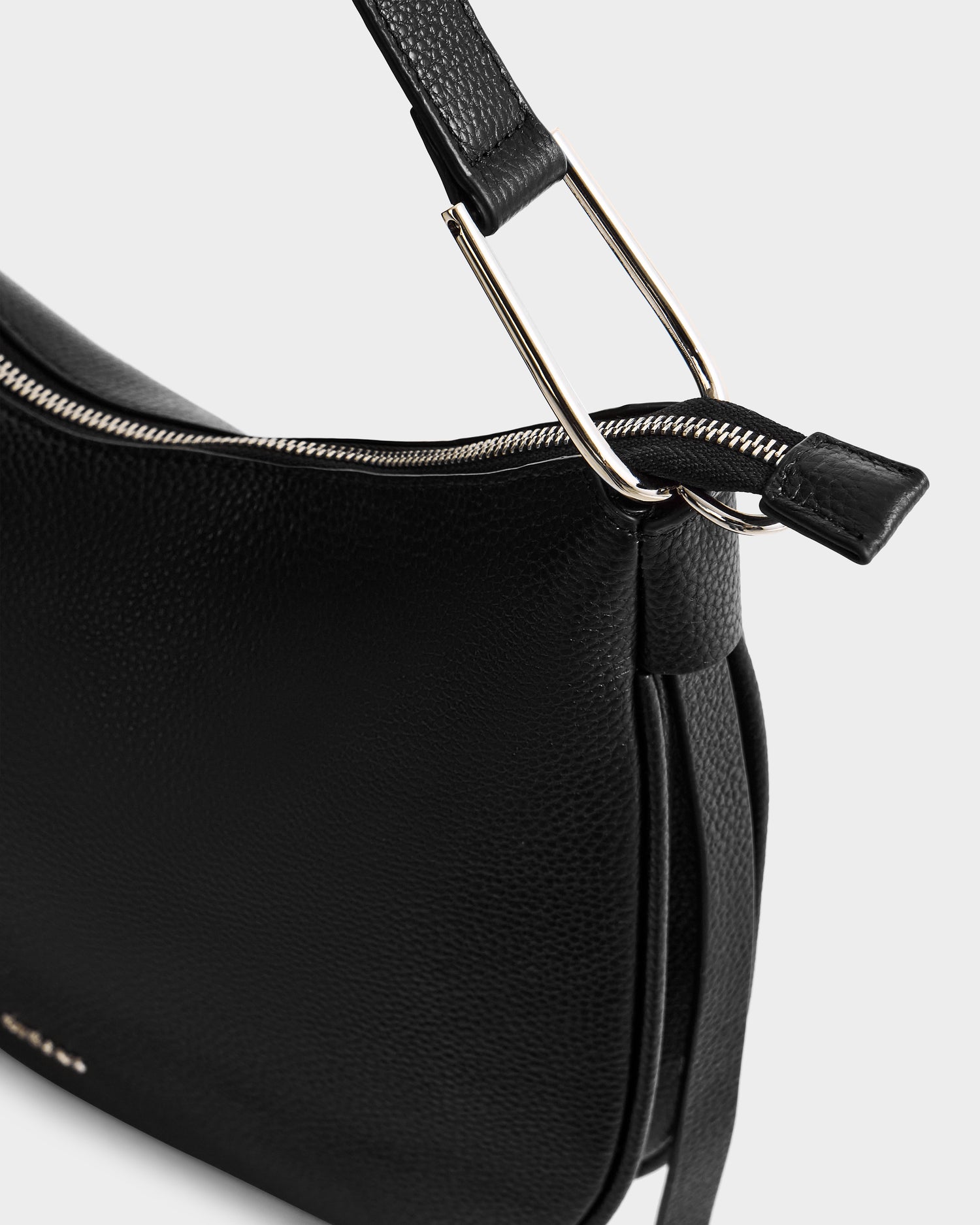 Close-up of the Rudsak SYLVIA - L325515 Black women’s leather shoulder bag featuring a textured finish, silver zipper, and metal handle hardware, set against a light gray background.