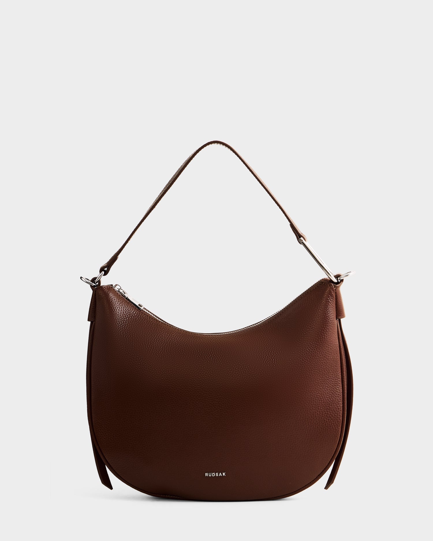 The SYLVIA - L325515 Mocha by Rudsak is a brown leather crescent bag with a minimalist curved design, single top handle, and silver zipper closure, ideal as a women's shoulder bag, shown on a plain white background.