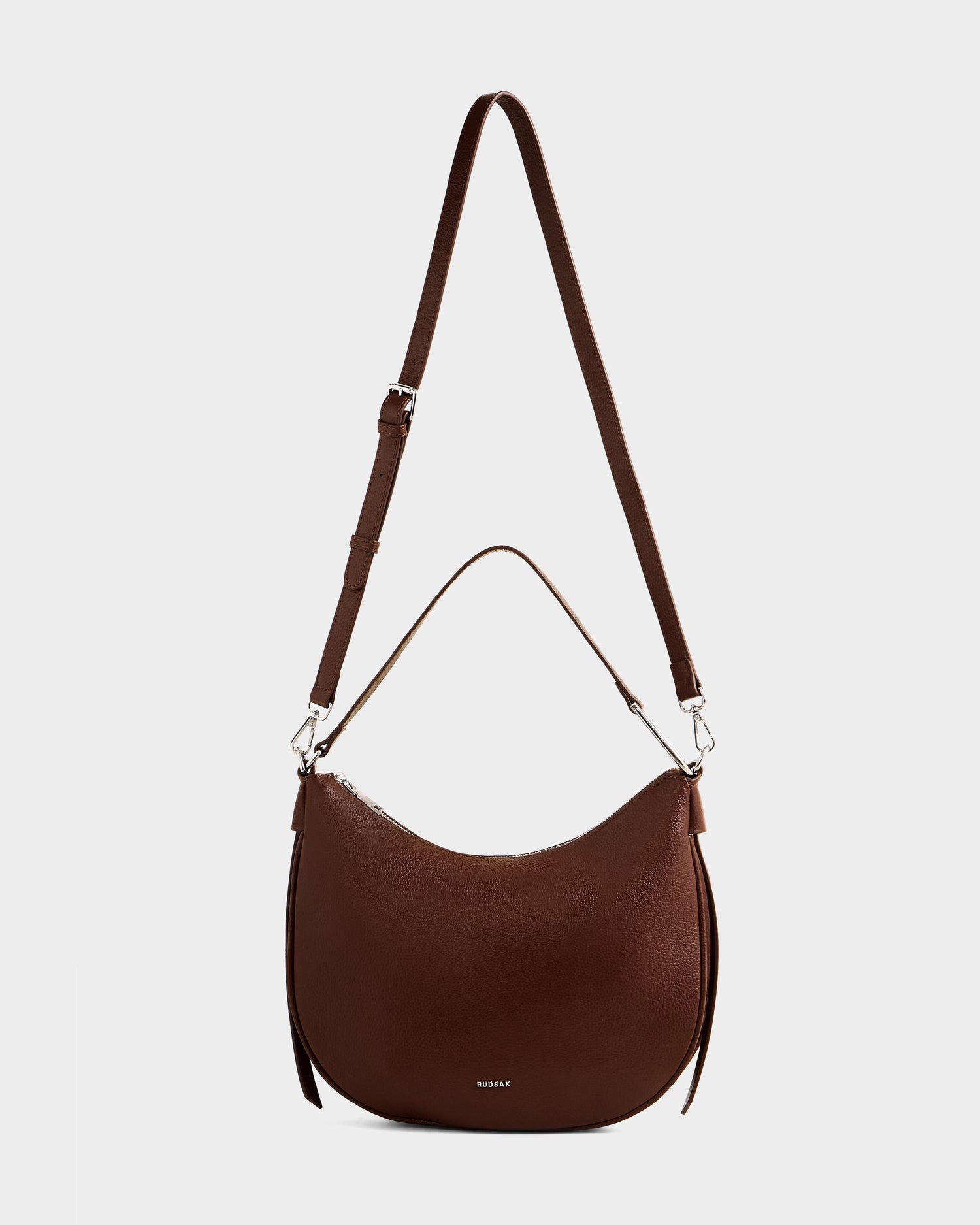 The Rudsak SYLVIA - L325515 Mocha is a women’s brown leather shoulder bag with a crescent shape, adjustable long strap, and short handle, shown on a plain white background.