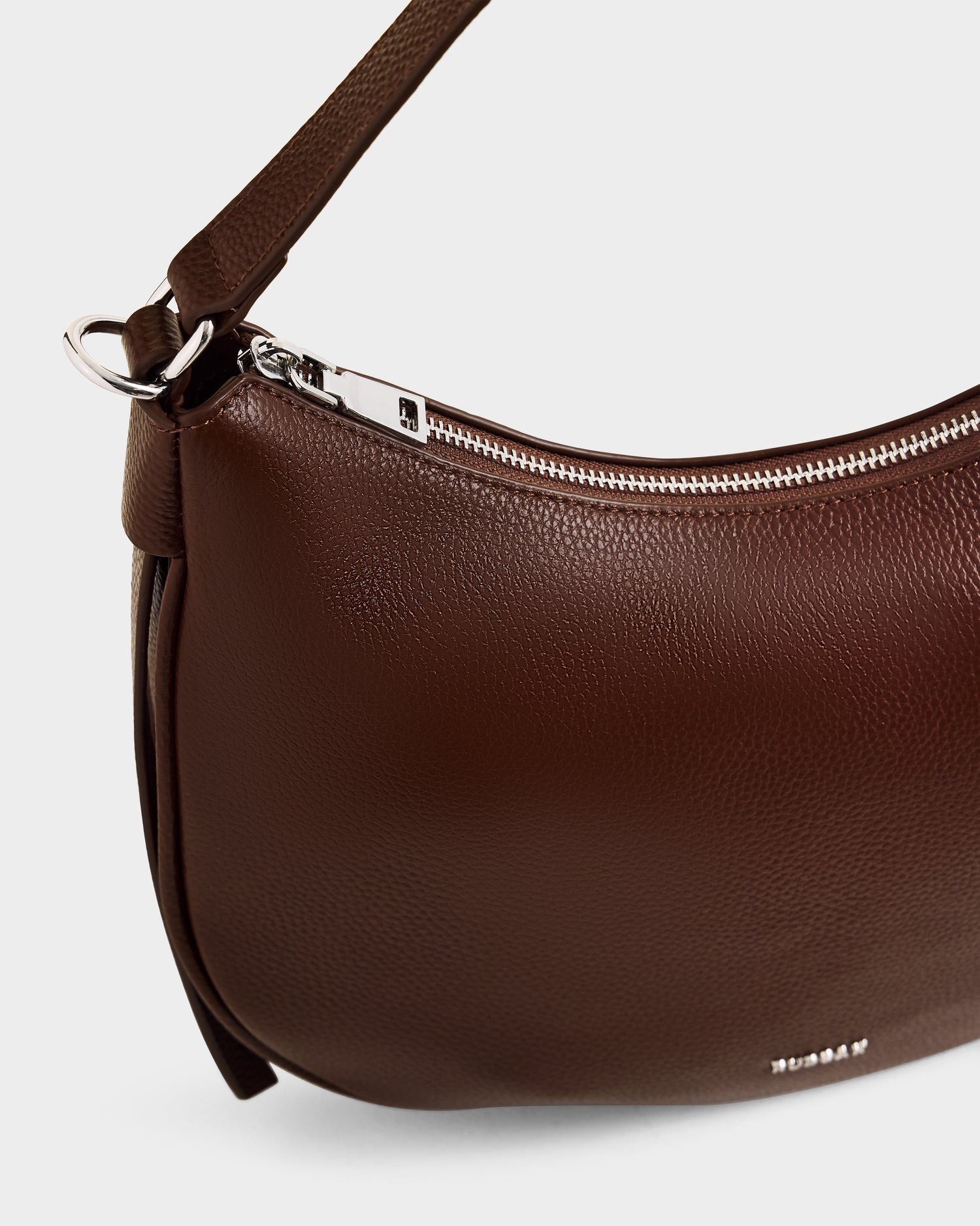 A close-up of the Rudsak SYLVIA - L325515 Mocha women’s leather shoulder bag, featuring a pebbled texture, silver zipper, and matching strap in a minimalistic design, set against a light background.