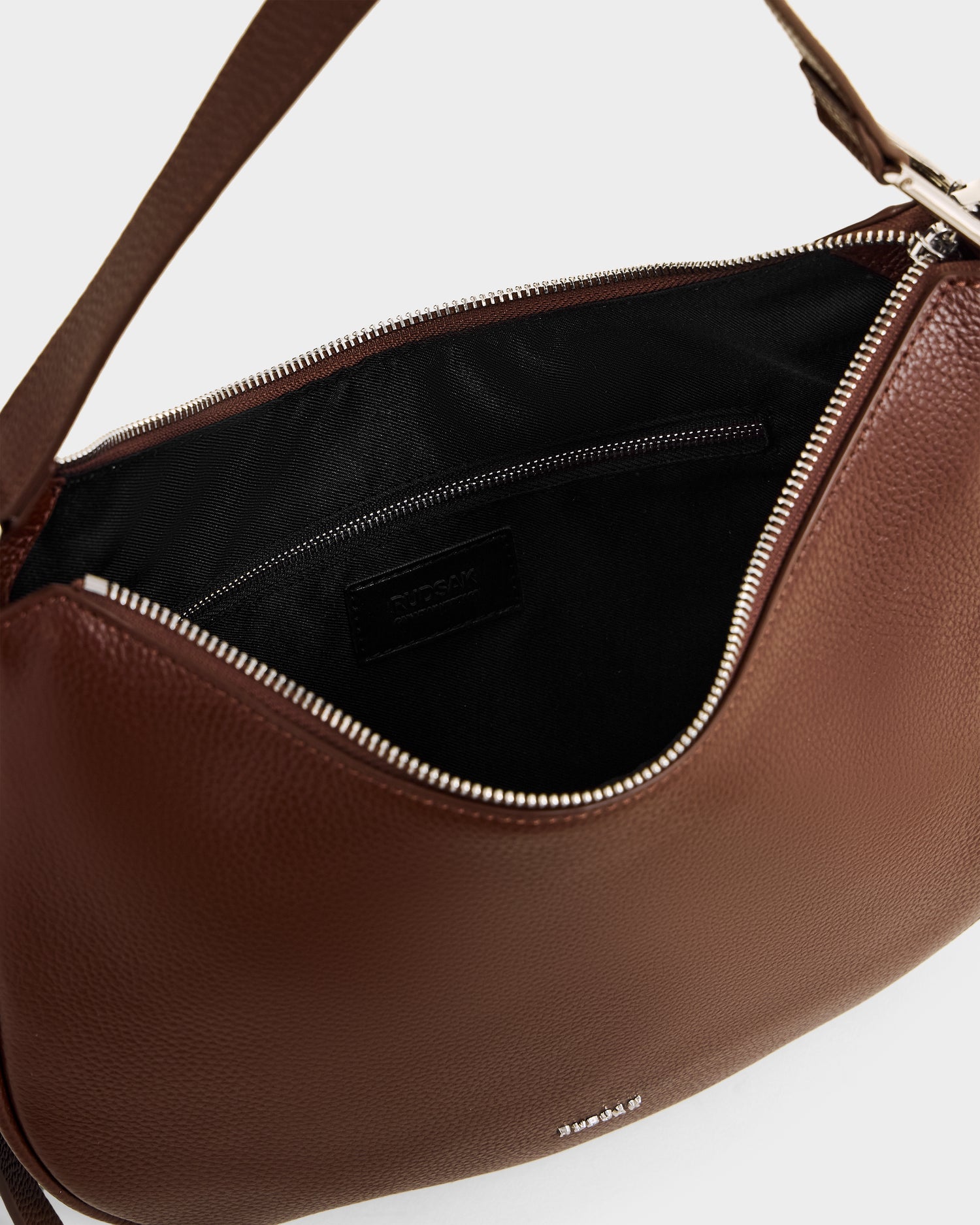 A close-up of the Rudsak SYLVIA - L325515 Mocha women’s leather shoulder bag in a crescent shape, shown open with a zipper closure, black fabric lining, and an inner zippered pocket.