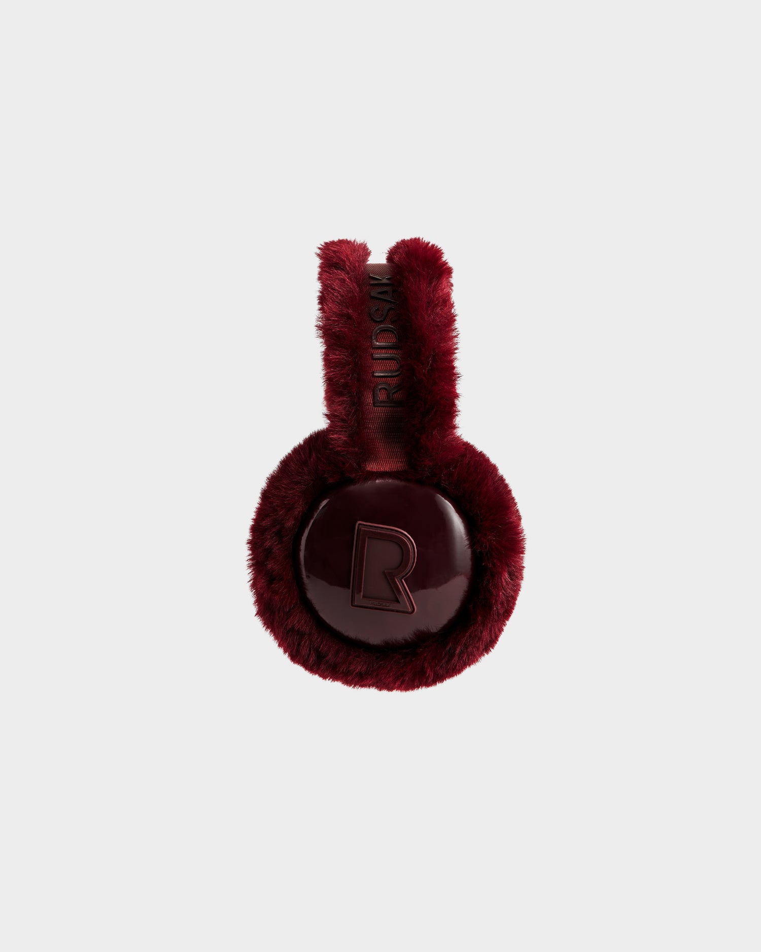 VALENCIA - 8425543 Bordeaux by Rudsak features burgundy faux fur earmuffs with glossy circular ear coverings embossed with "R" and "RUSLAN" on the headband, styled as a chic winter accessory against a plain light background.