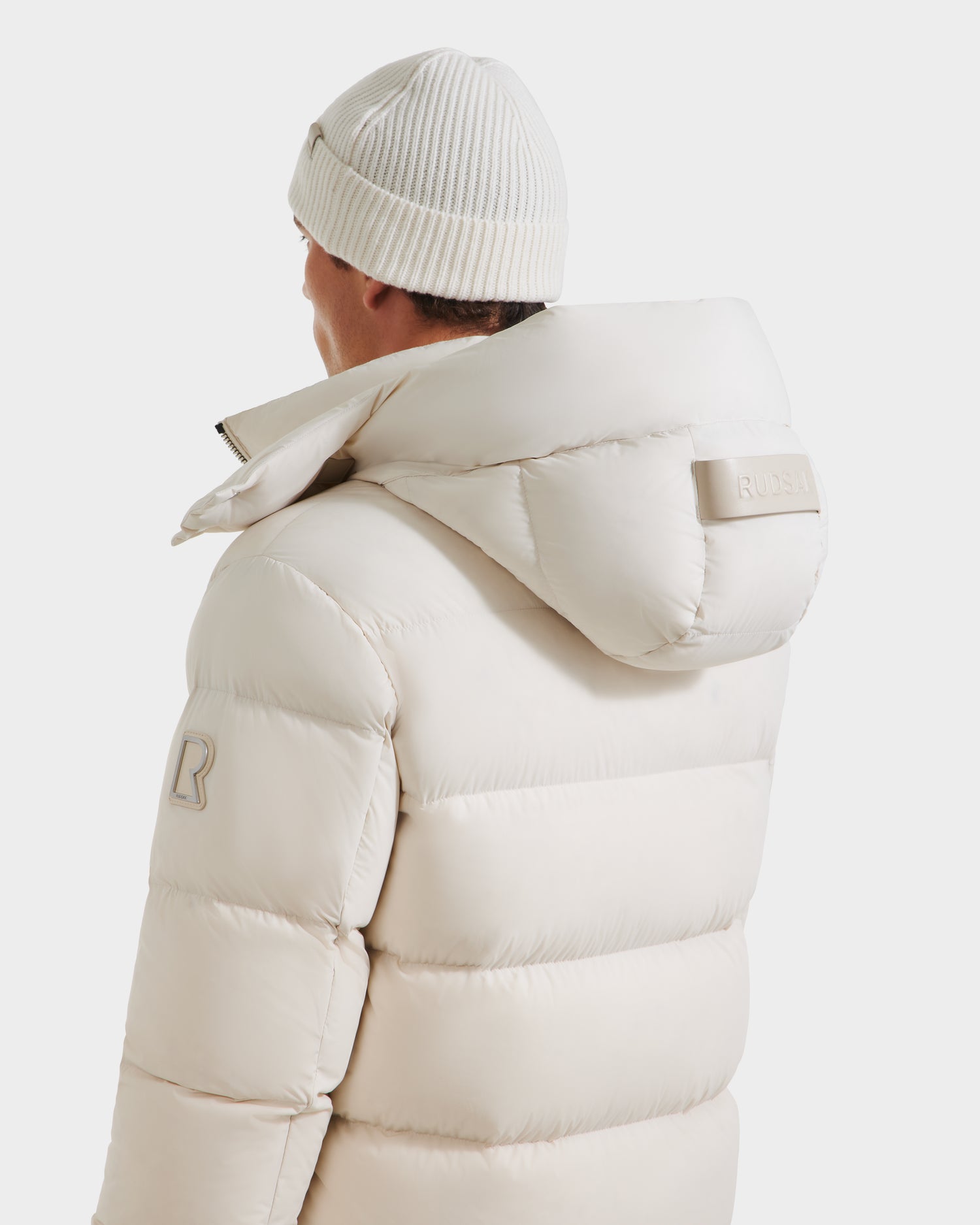 A person is seen from behind wearing a Rudsak VINCE M - 6124561 Vanilla mens quilted down puffer with RDS-certified fill and a white beanie, set against a plain white background.