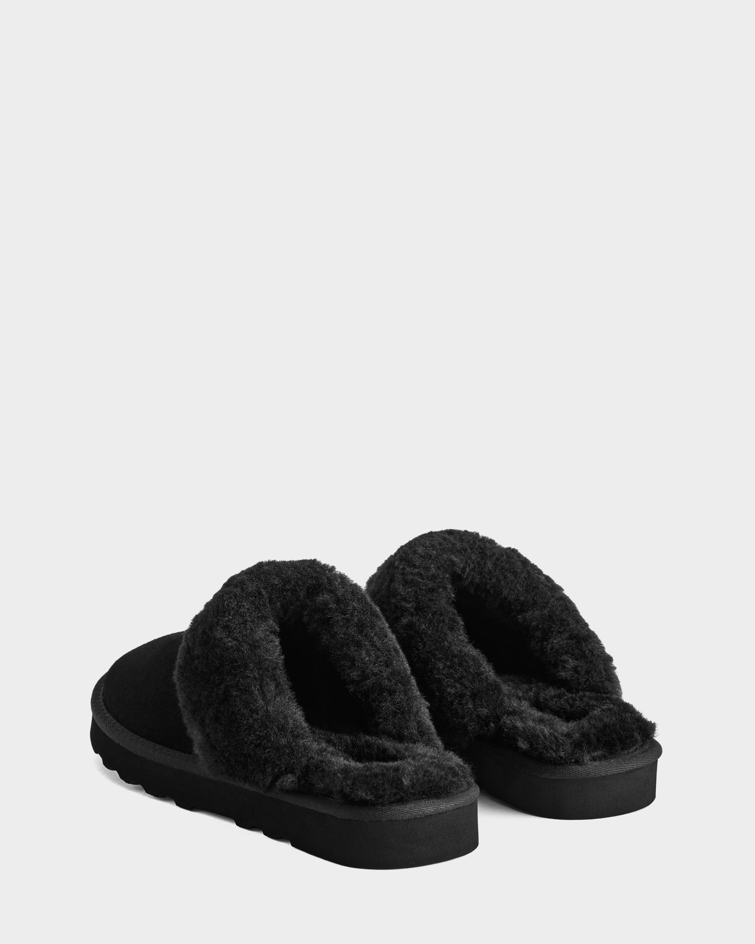 The Rudsak WILBER - 6225509 Black men's backless suede slippers with thick faux shearling fleece lining and sturdy soles are angled on a white background—ideal for comfortable, stylish loungewear.