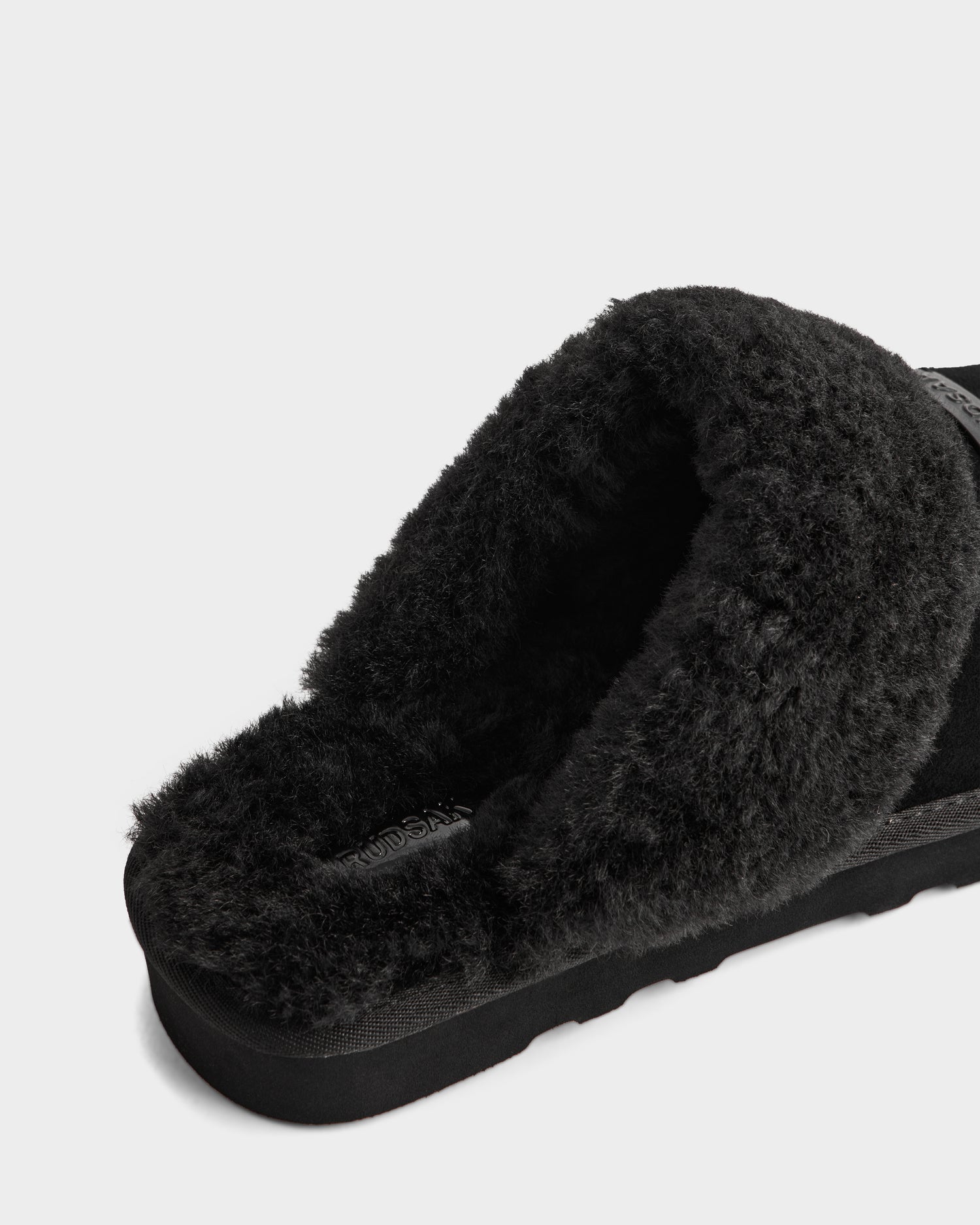 A close-up of the Rudsak WILBER - 6225509 Black men's suede slipper, lined with plush faux shearling, highlights its cozy interior and sole—ideal loungewear displayed on a plain white background.