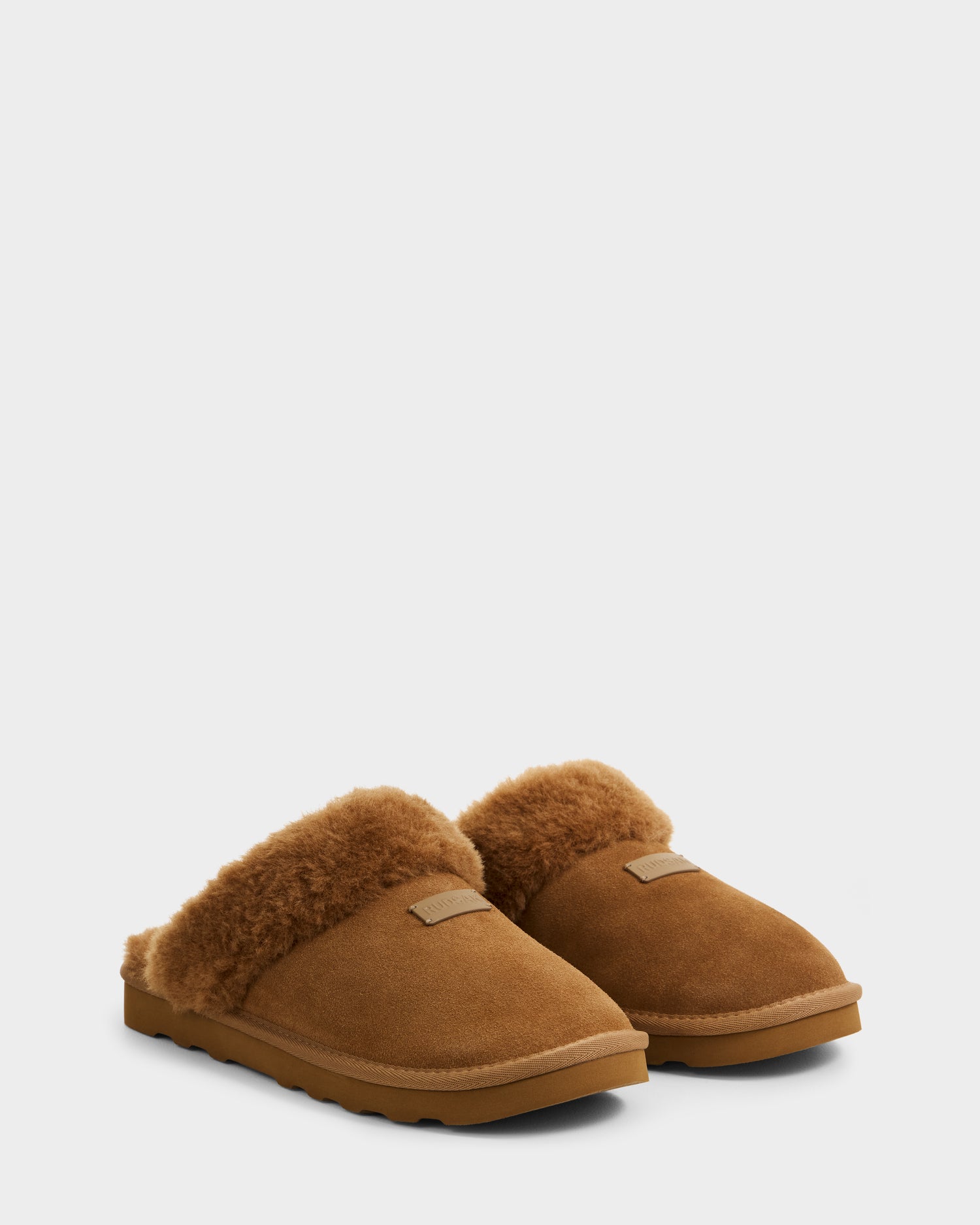 The Rudsak WILBER - 6225509 Tan men’s suede slippers feature a plush faux shearling lining and durable rubber soles, perfect for relaxing at home, shown here in brown against a plain white background.