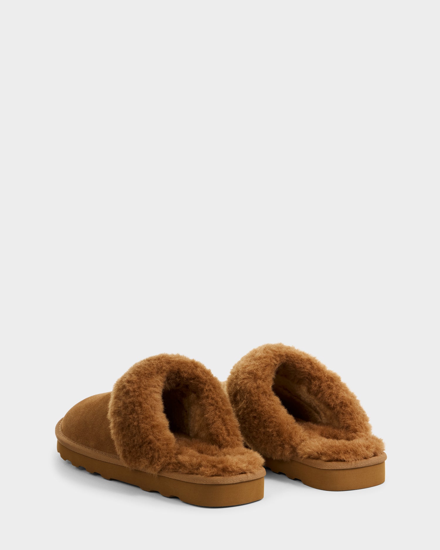 The Rudsak WILBER - 6225509 Tan men’s suede slippers feature a fluffy faux shearling lining and textured sole, ideal for cozy loungewear. Shown from the back and side on a white background.
