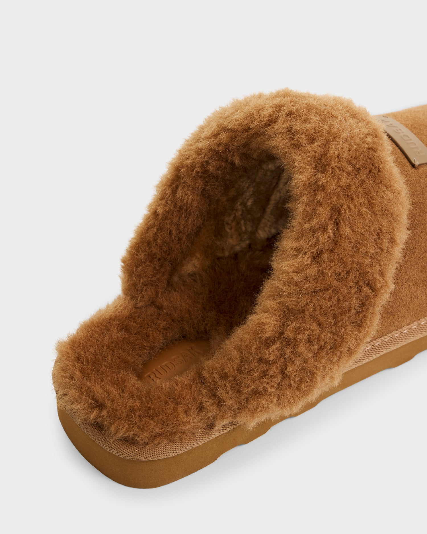 A close-up of the Rudsak WILBER - 6225509 Tan men’s suede slipper with a soft faux shearling lining and sturdy sole, shown against a plain white background.