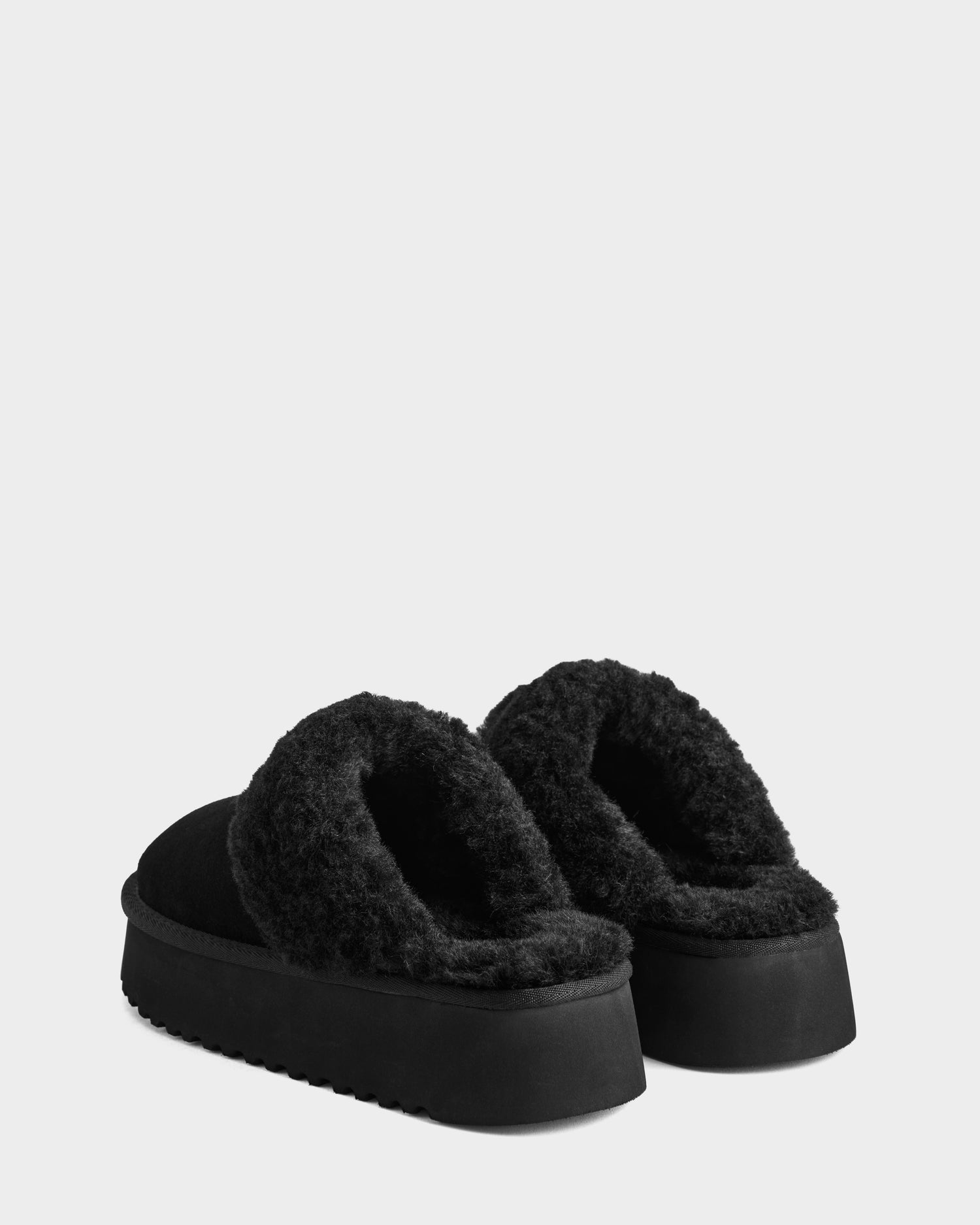 The Rudsak WILMA - 8225582 Black women’s slippers feature thick textured soles and plush interiors for cozy winter style, shown against a light gray background.