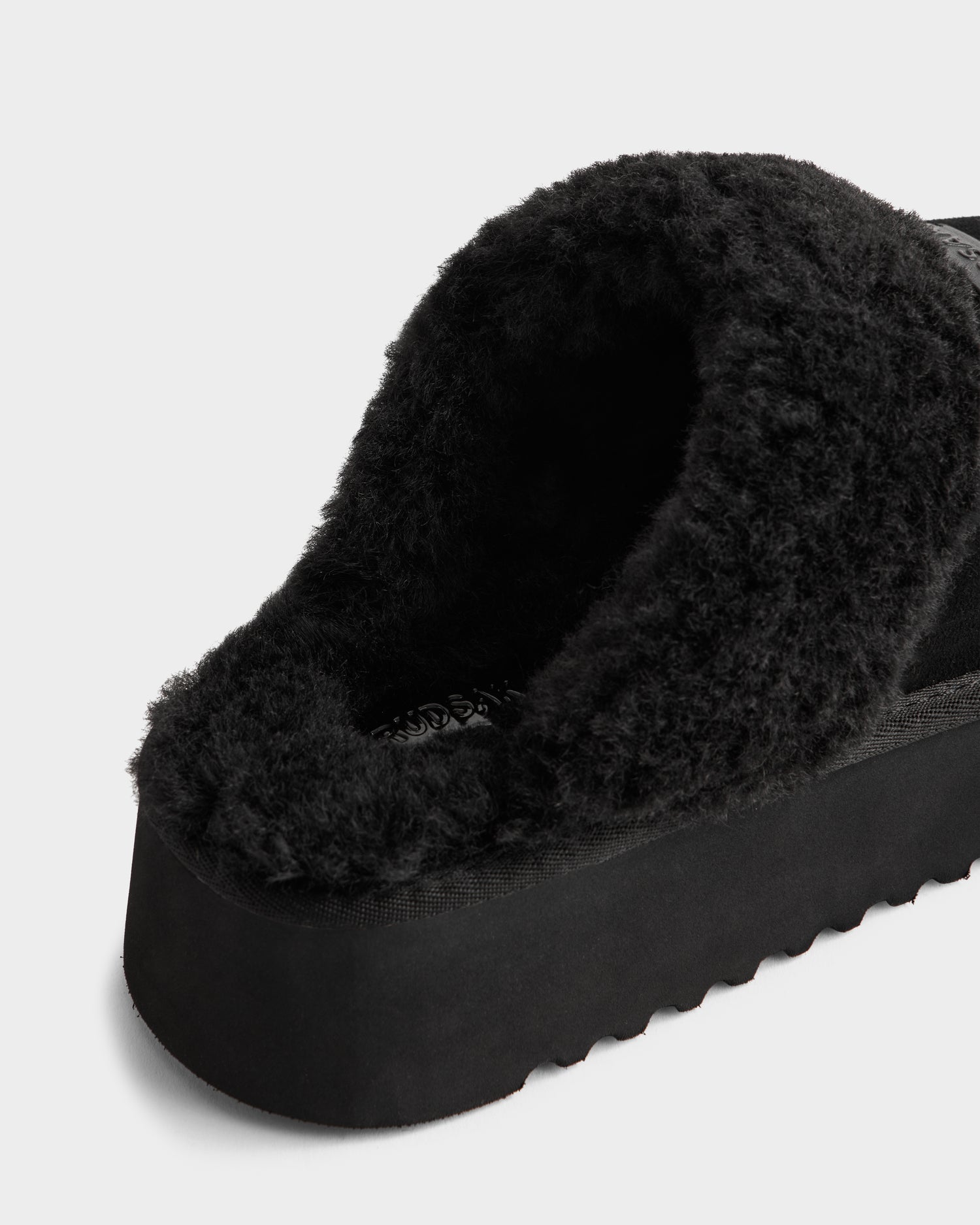 Close-up of the heel and interior of the WILMA - 8225582 Black women’s slipper by Rudsak, featuring a thick, fuzzy lining and chunky textured sole—ideal for winter—set against a plain white background.