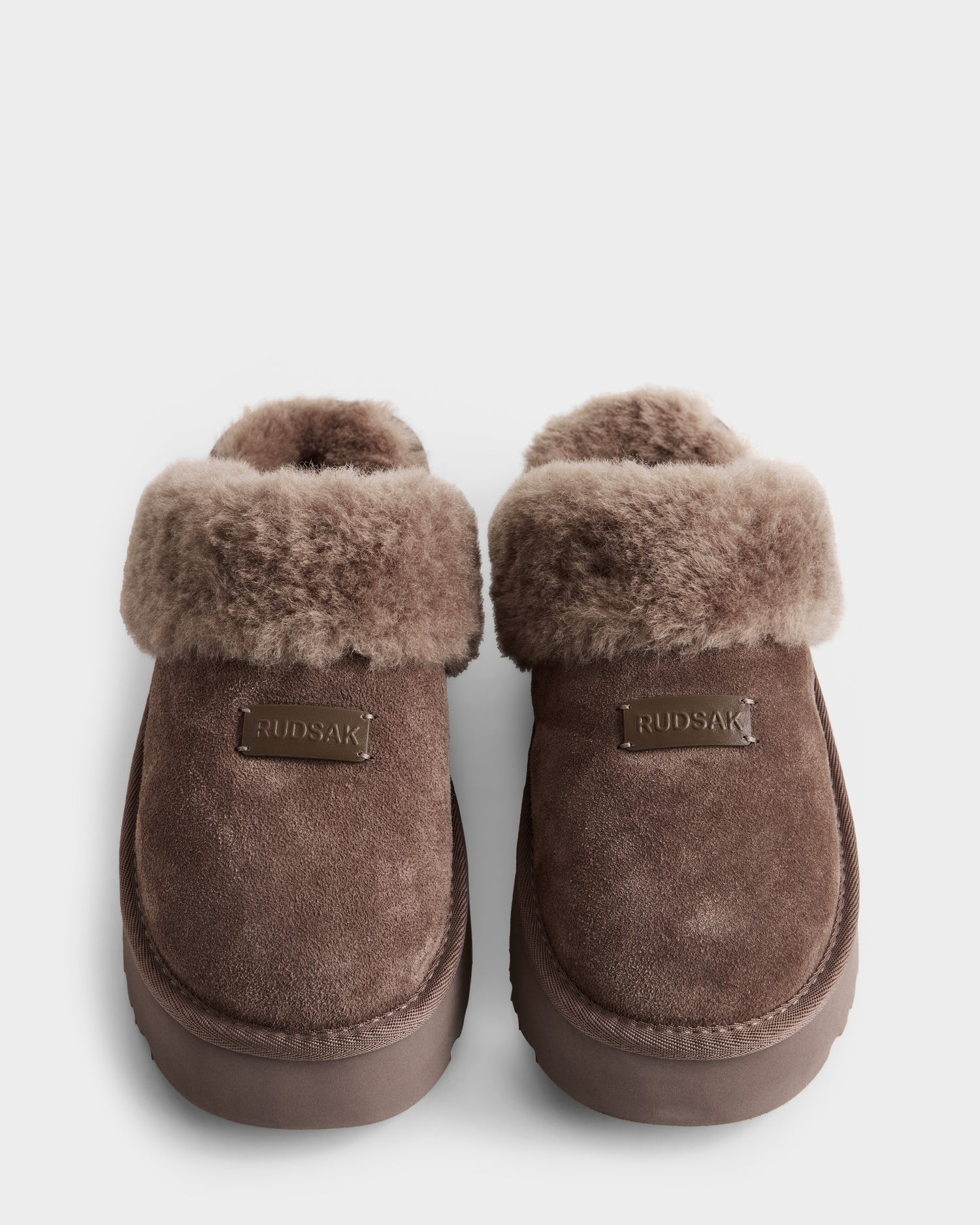 A pair of WILMA - 8225582 Mocha brown suede slippers by Rudsak with plush fuzzy cuffs, platform sole, and front brand tags, shown from above on a white background.