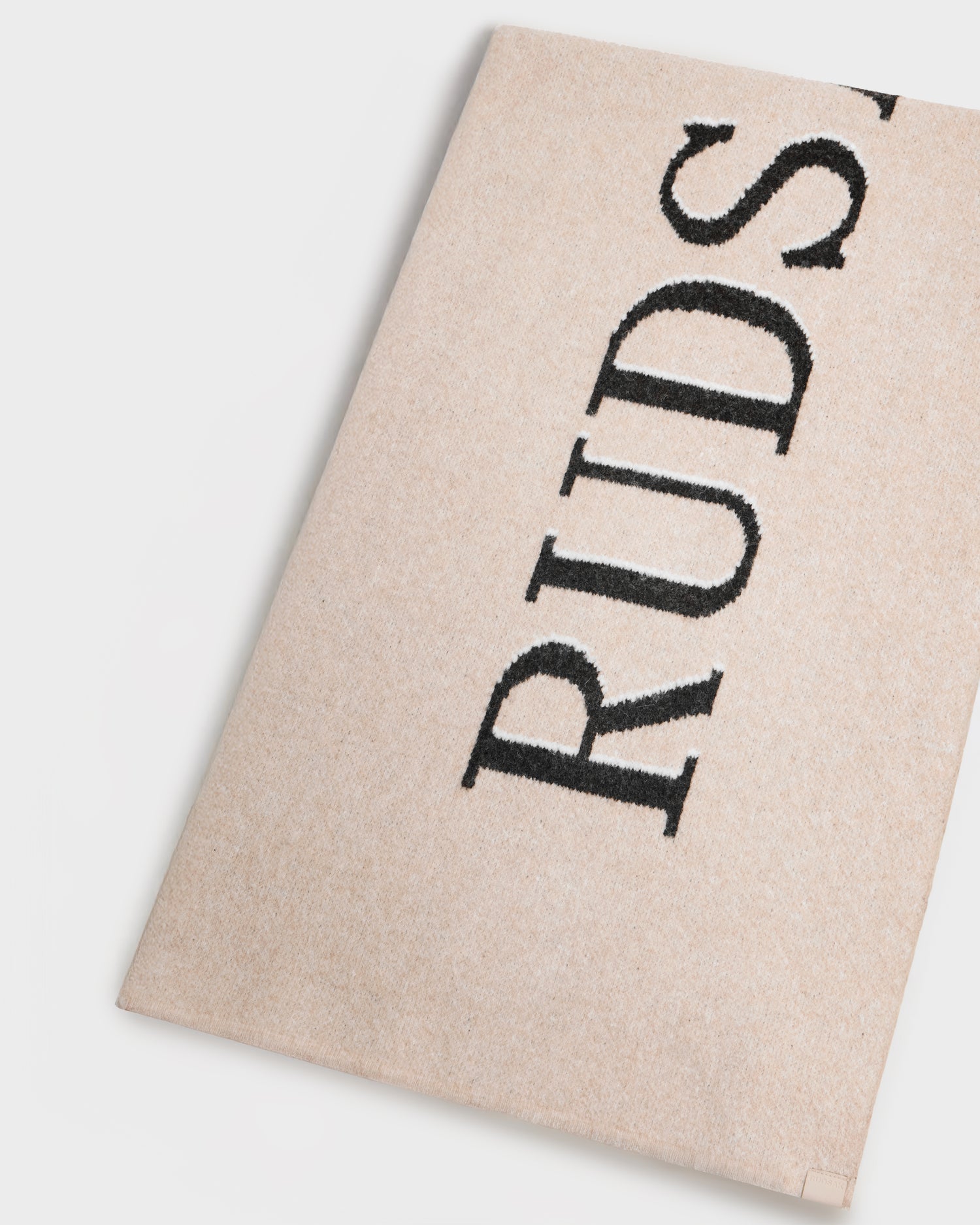 A beige textured surface shows partial vertical black "RUDS" text, photographed on white. It’s the WYATT - 6425039 Vanilla scarf by Rudsak—a men’s winter essential combining style and warmth.