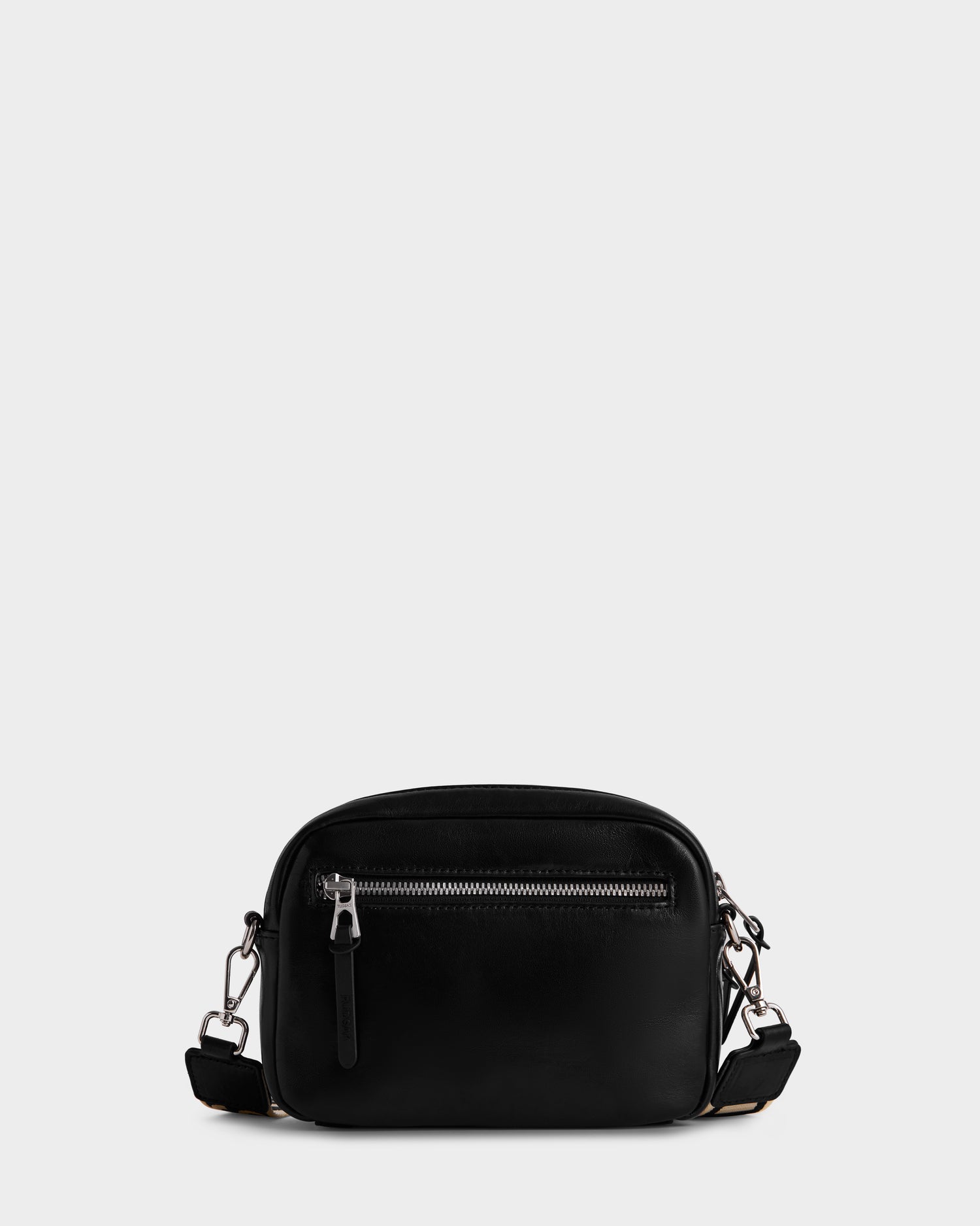 The Rudsak ZOYA L - 8325543 Black is a small black crossbody bag in smooth leather, with a front zip pocket, silver hardware, and an adjustable logo strap, shown against a plain light gray background.