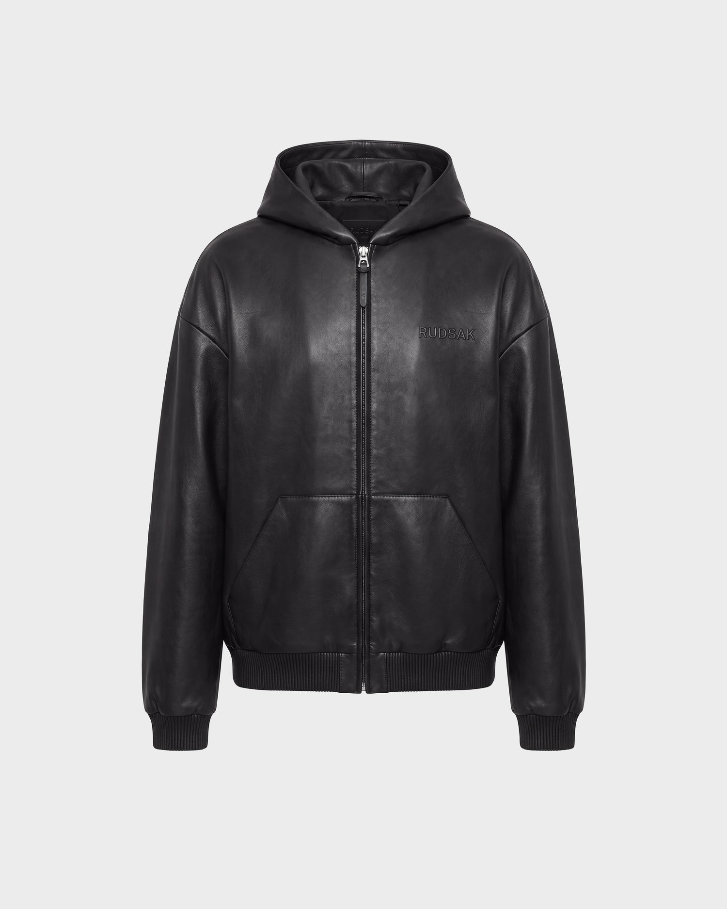ARCHIE - 6126500 Black leather hoodie by Rudsak, featuring a front zipper, ribbed cuffs and hem, and two front pockets, displayed against a plain light gray background. The Rudsak logo is embossed on the left chest area, adding an urban touch to the stylish design.