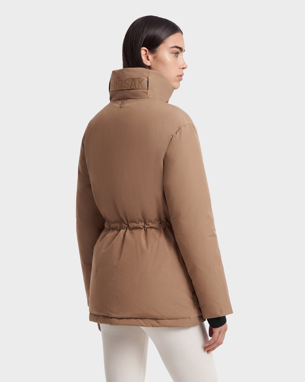 A model wears a Rudsak BHIMA - 8126515 Camel winter parka puffer jacket, featuring a cinched waist and a high collar with embossed lettering.