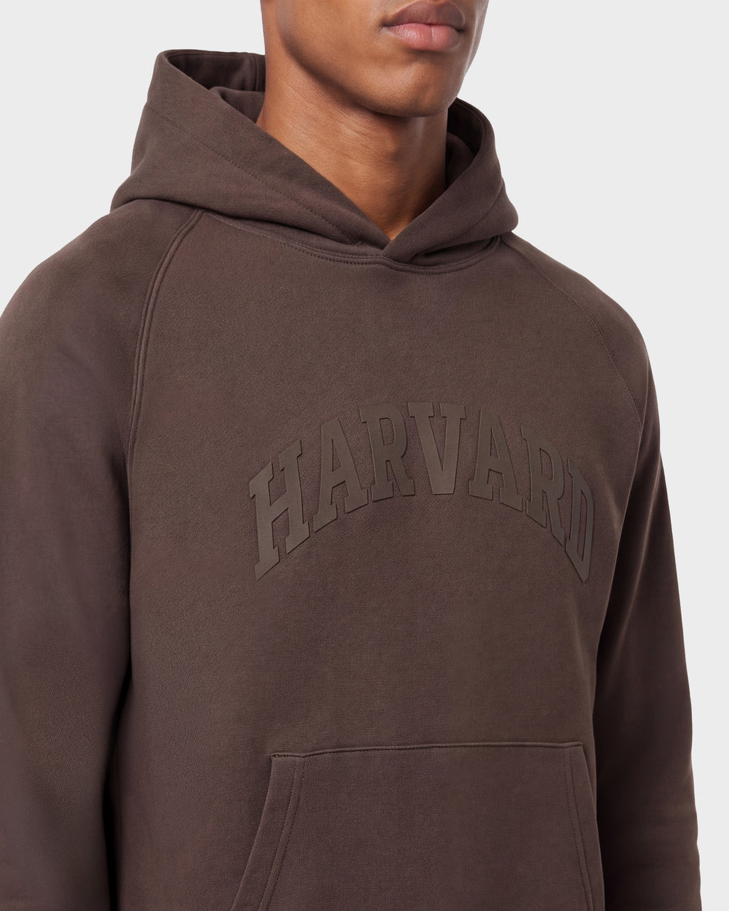 A person wearing the Rudsak BRIAR R HV - H525506 Espresso limited-edition brown hoodie, featuring an embossed HARVARD logo on the front and a front pocket, set against a plain light gray background.