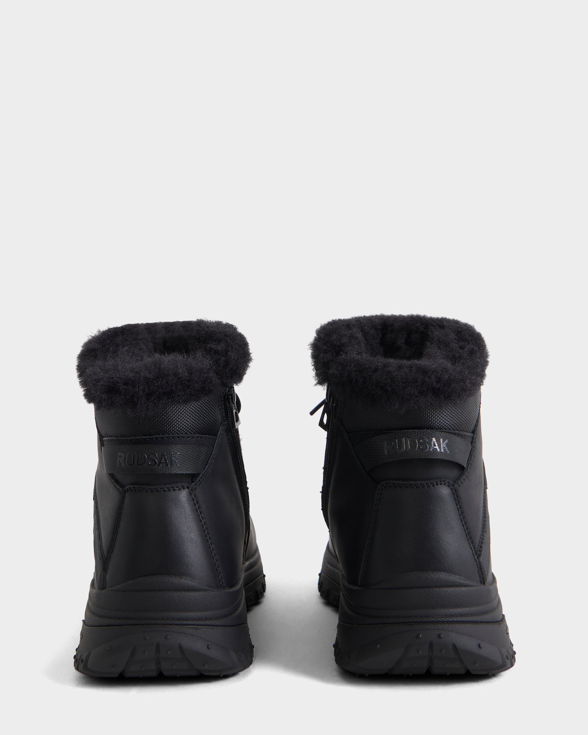 The BRYSON - 6226504 Black by Rudsak are black winter boots with fur trim and lace-up design, shown from the back on a white background. Both heels feature RUDSAK logos.