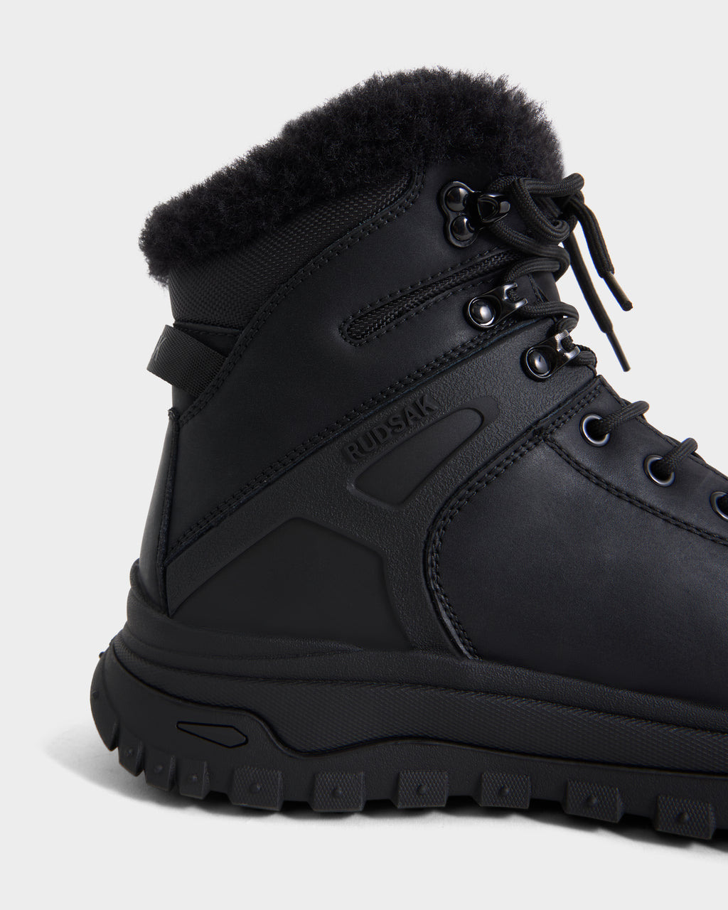 A close-up of the BRYSON - 6226504 Black winter boot featuring a fur lining, lugged outsole, and lace-up design with the Rudsak logo embossed on the side.
