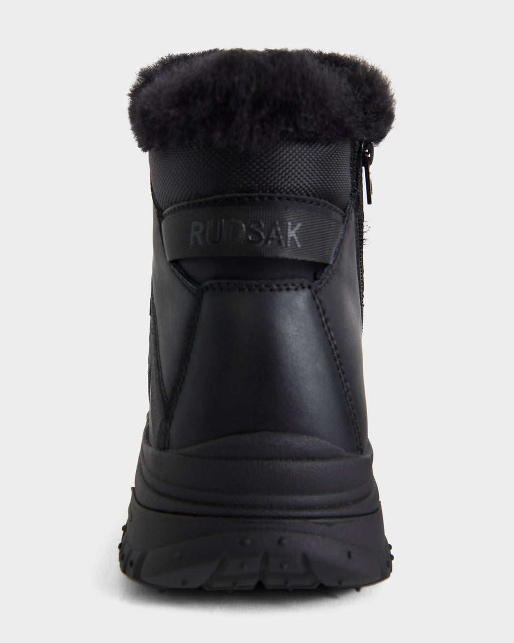 Back view of BRYSON - 6226504 Black by Rudsak: a black winter boot with thick lugged outsole, shearling cuff, side zipper, and RUDSAK logo on the heel, set against a plain white background.