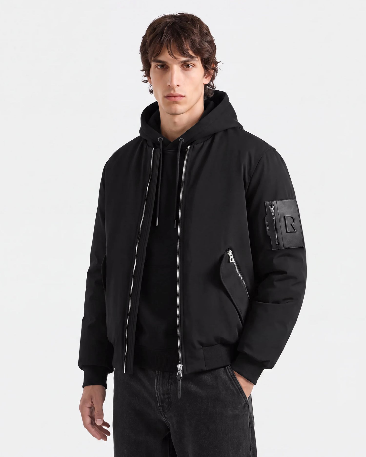 A person wearing the Rudsak DYLAN - 6125593 Black men’s aviator bomber jacket, which features zippered pockets and a removable faux fur collar, paired with dark pants, stands against a plain white background looking at the camera with a neutral expression.