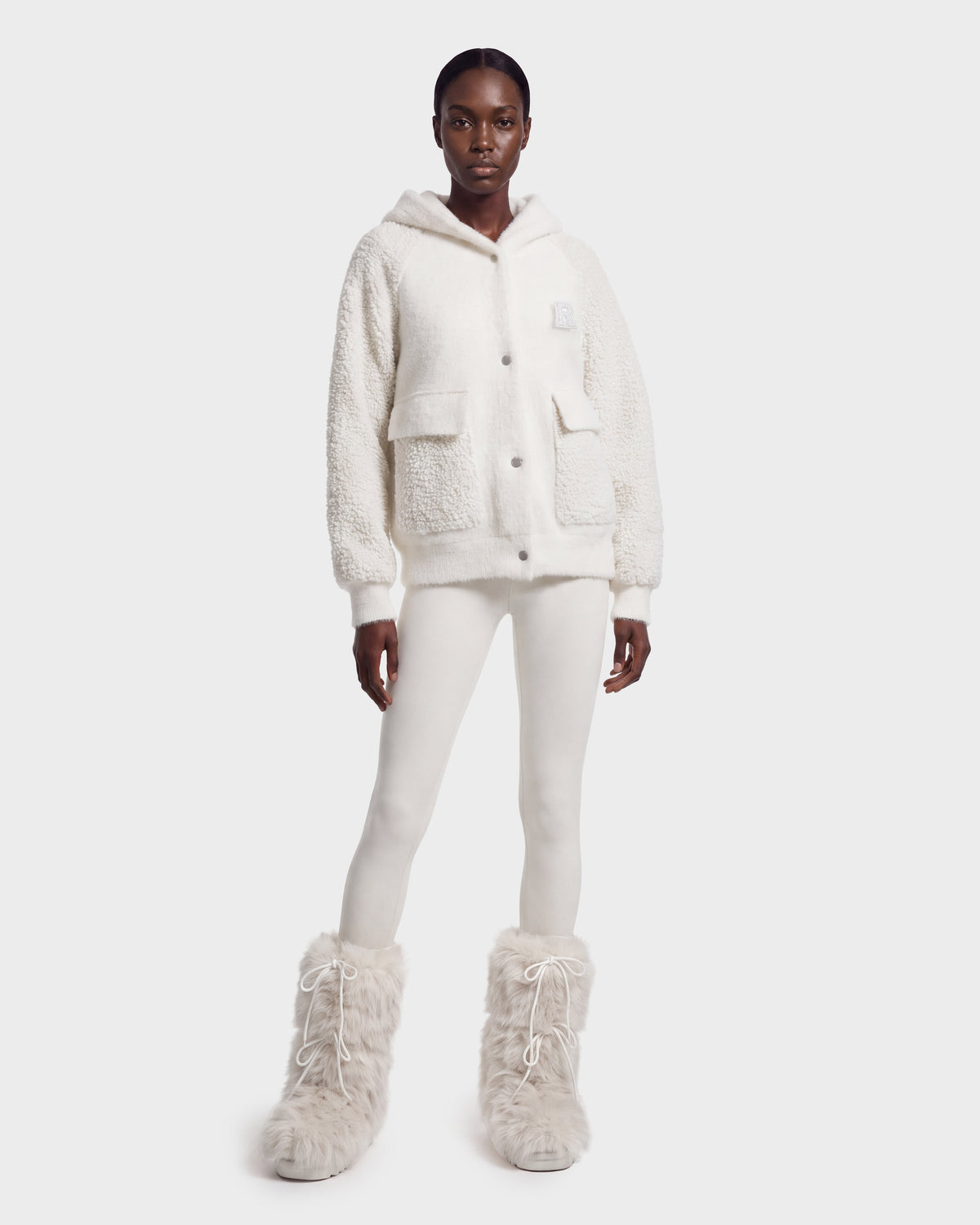 A person wearing the DAKOTA - 8526515 Iceland by Rudsak stands facing forward in white pants and fuzzy boots, creating a stylish cold-weather look against a plain white background.