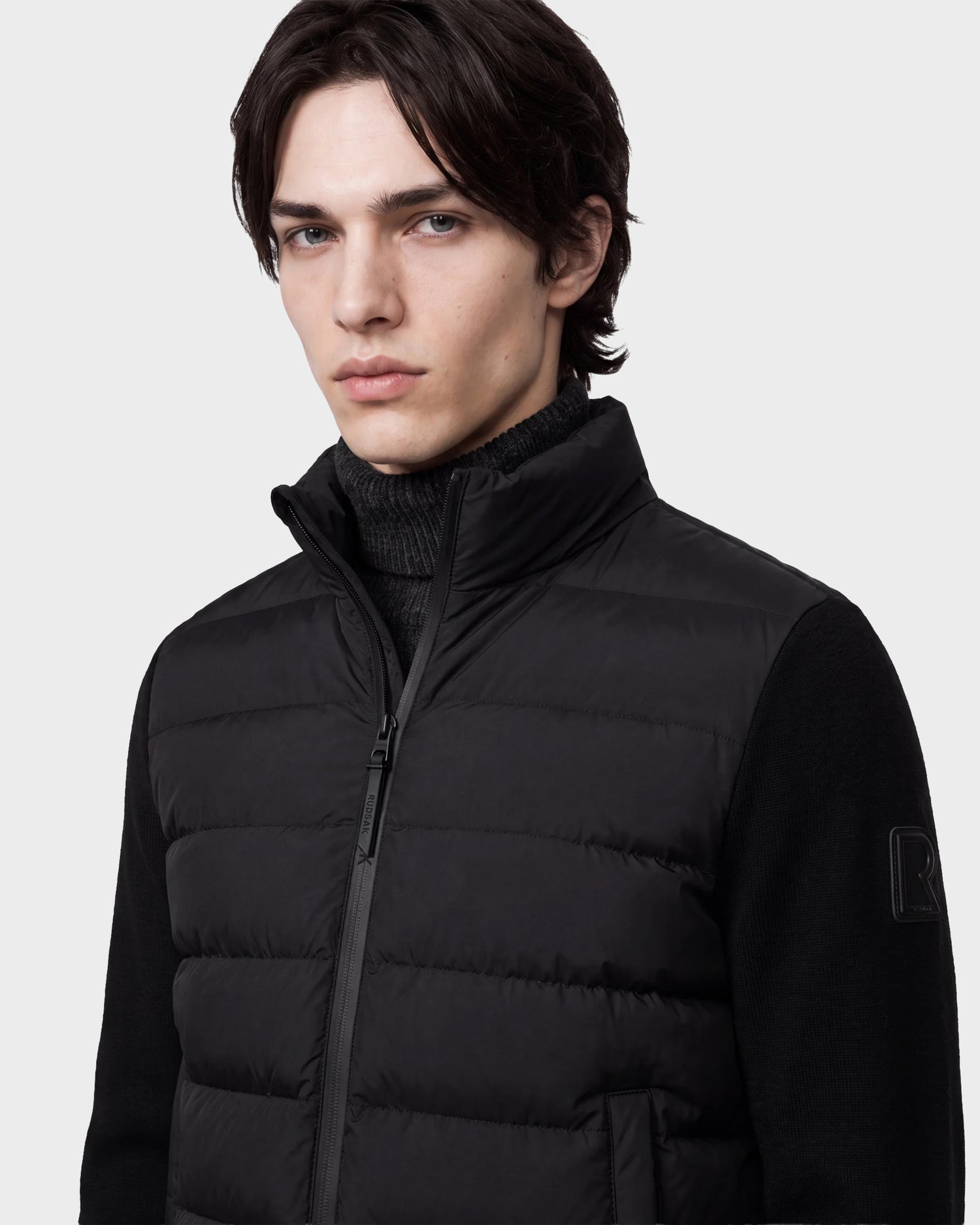 A young person with medium-length dark hair wears the Rudsak EUGENE - 6124721 Black lightweight mixed-media jacket over a black sweater, looking at the camera with a neutral expression against a plain background.