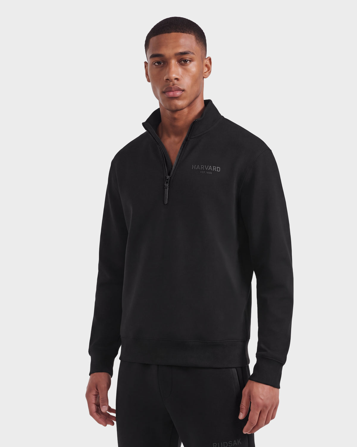 A man stands facing forward, wearing the Rudsak FREMONT HV - H525501 Black unisex pullover and matching black pants against a plain light background.
