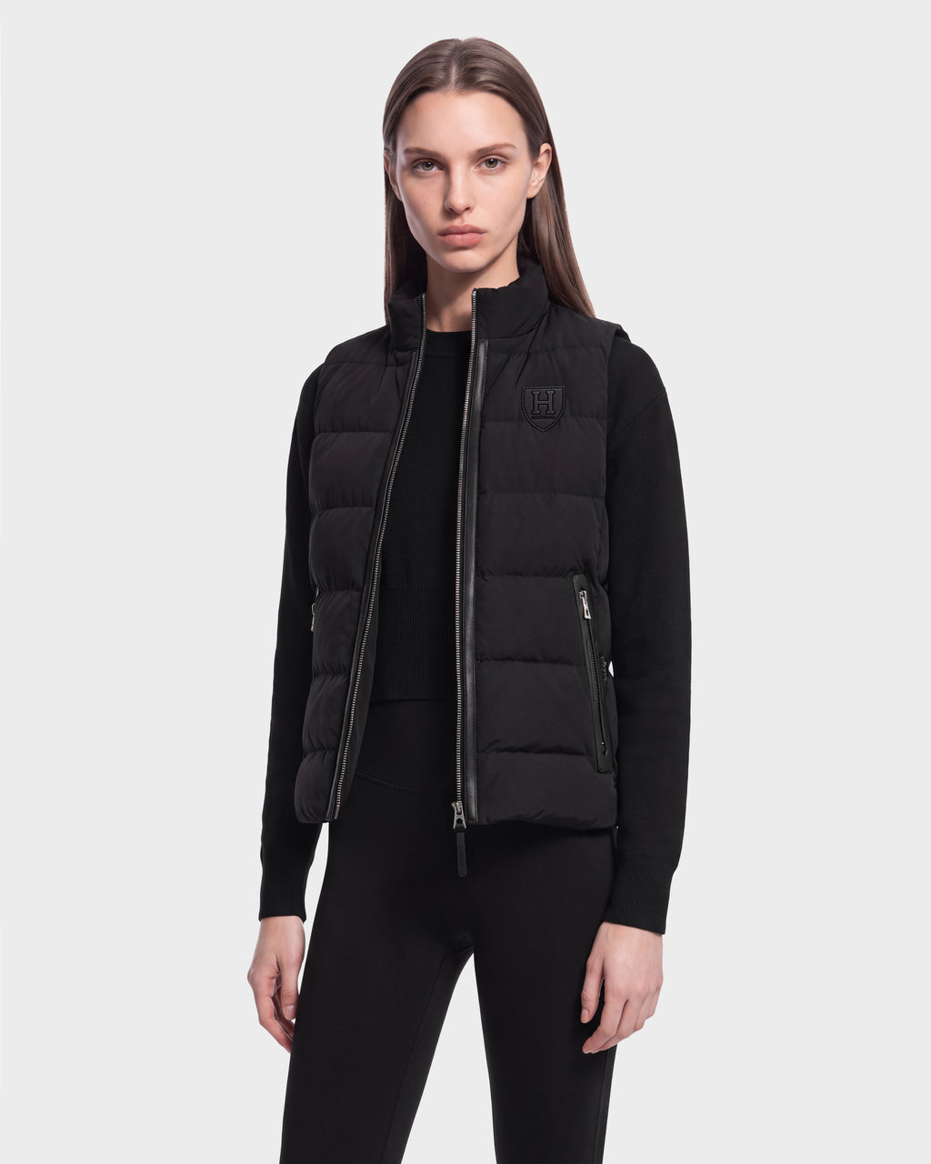 A person wearing the Rudsak GABRIELA HV - H125507 Black puffer vest over a black long-sleeve top and black pants stands facing forward against a plain light background.