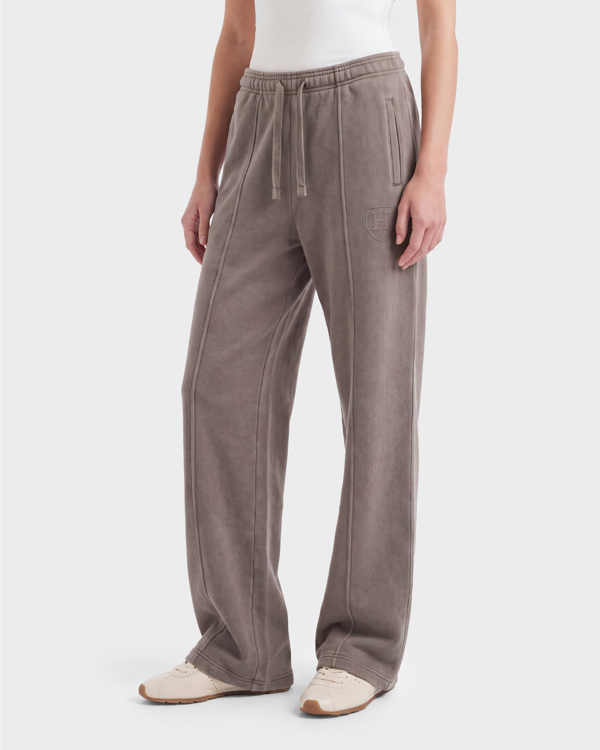 A person wearing Rudsak GAELLE HV - H526902 Taupe heavyweight jersey jogger sweatpants with a drawstring waist and side pockets, paired with a white top and beige sneakers, stands against a plain white background.