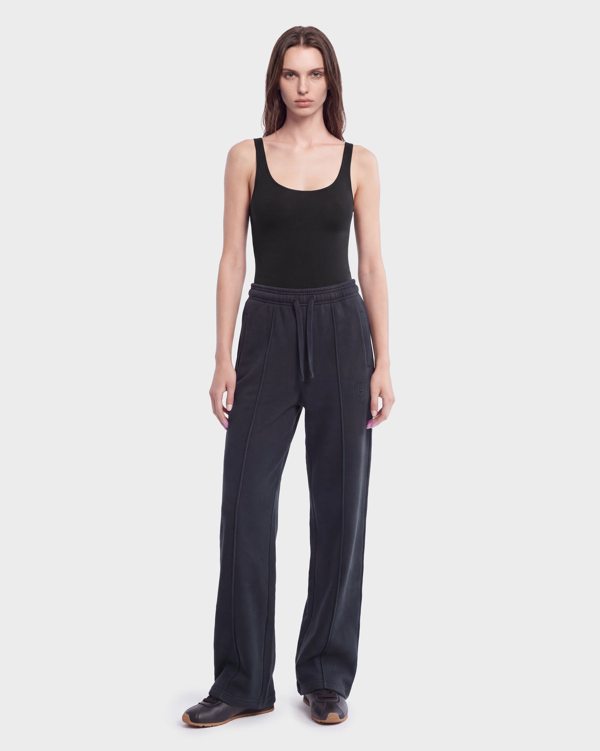 A person stands facing forward, wearing Rudsak’s GAELLE HV - H526902 Titanium black sleeveless top and loose, dark heavyweight jersey jogger pants with black shoes. The background is plain white.