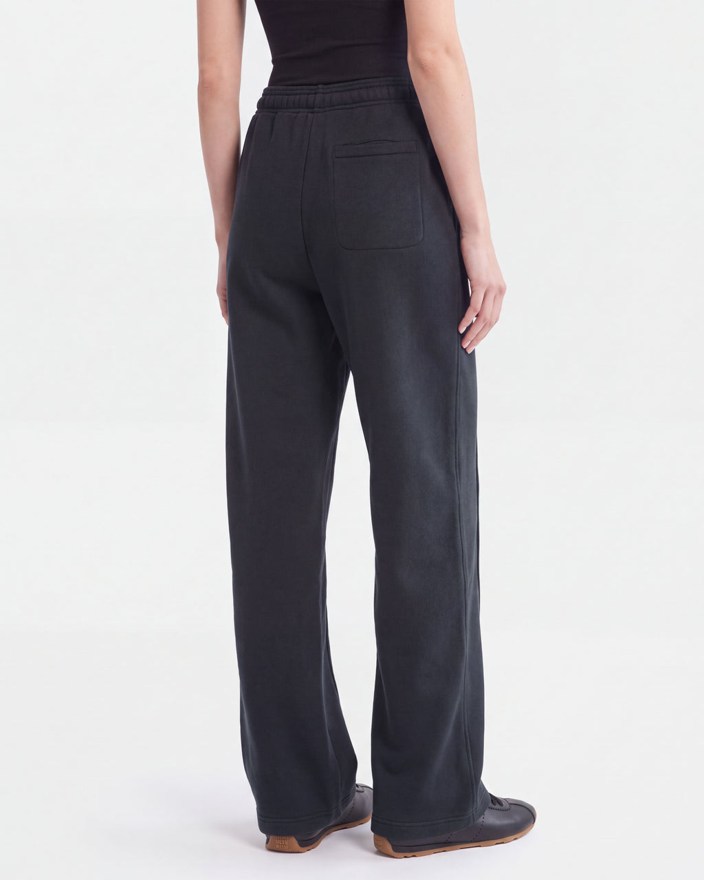 A person wearing loose-fitting black heavyweight jersey jogger pants, the GAELLE HV - H526902 Titanium by Rudsak, and a black top stands facing away, showcasing the back pocket on the pants. The style expresses classic RUDSAK minimalism against a plain white background.