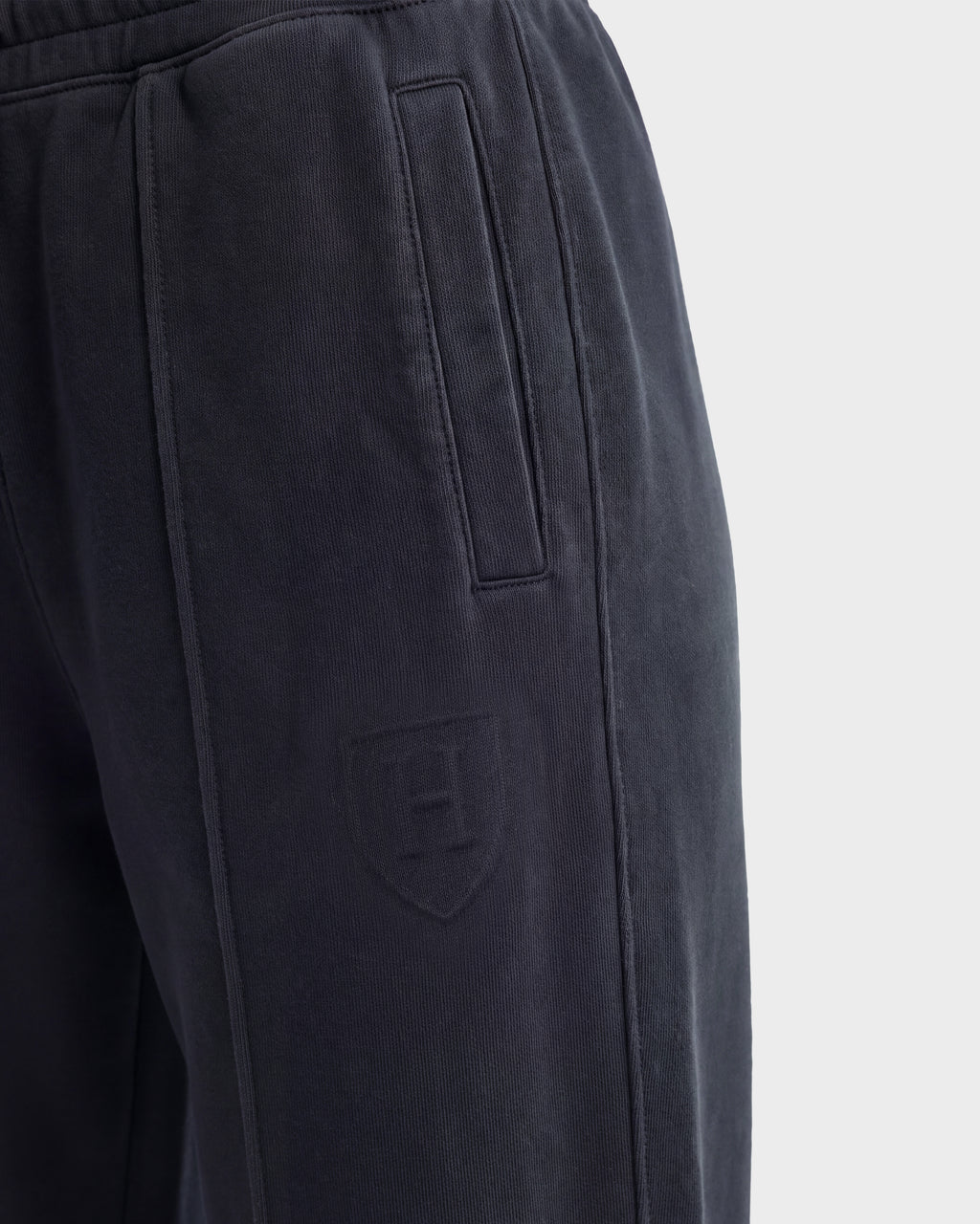 Close-up of Rudsak’s GAELLE HV - H526902 Titanium heavyweight jersey jogger sweatpants in black, showcasing a vertical pocket and an embossed shield logo with the letter H on the upper thigh. The fabric appears soft and slightly textured.