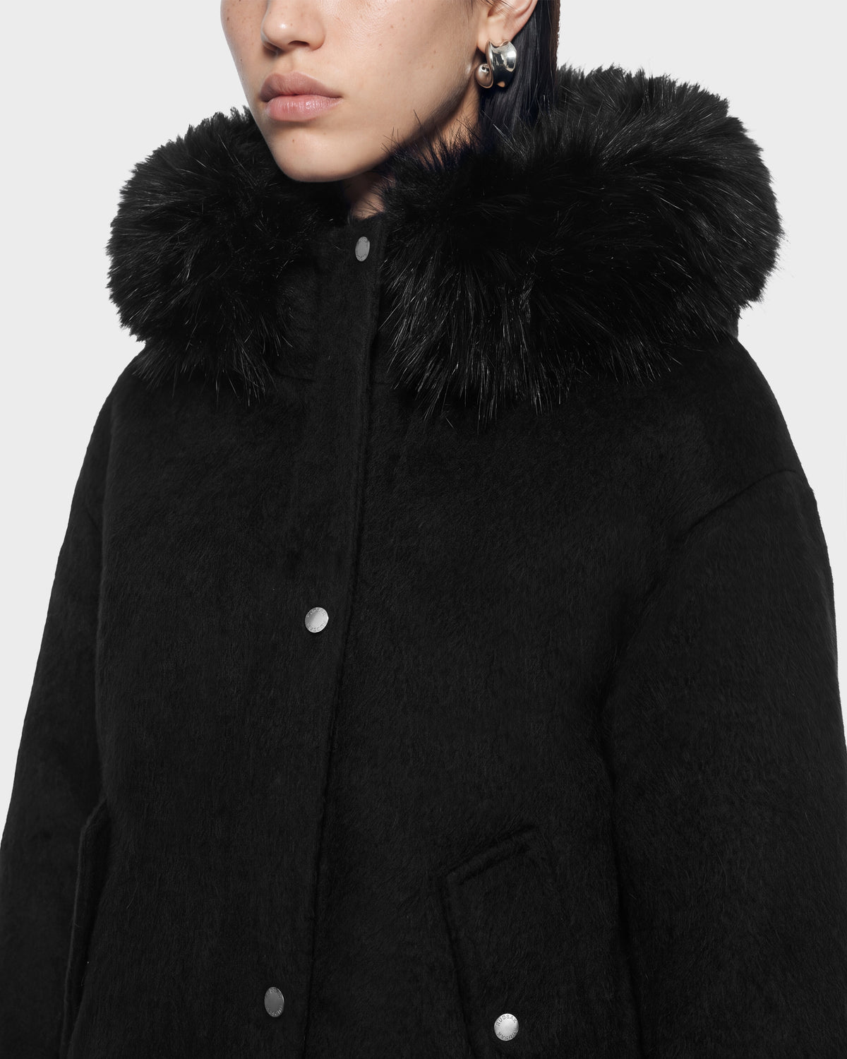 Close-up of a person wearing a black HAZEL - 8126981 Black wool-blend winter coat with a thick faux-fur trim hood and silver snap buttons.