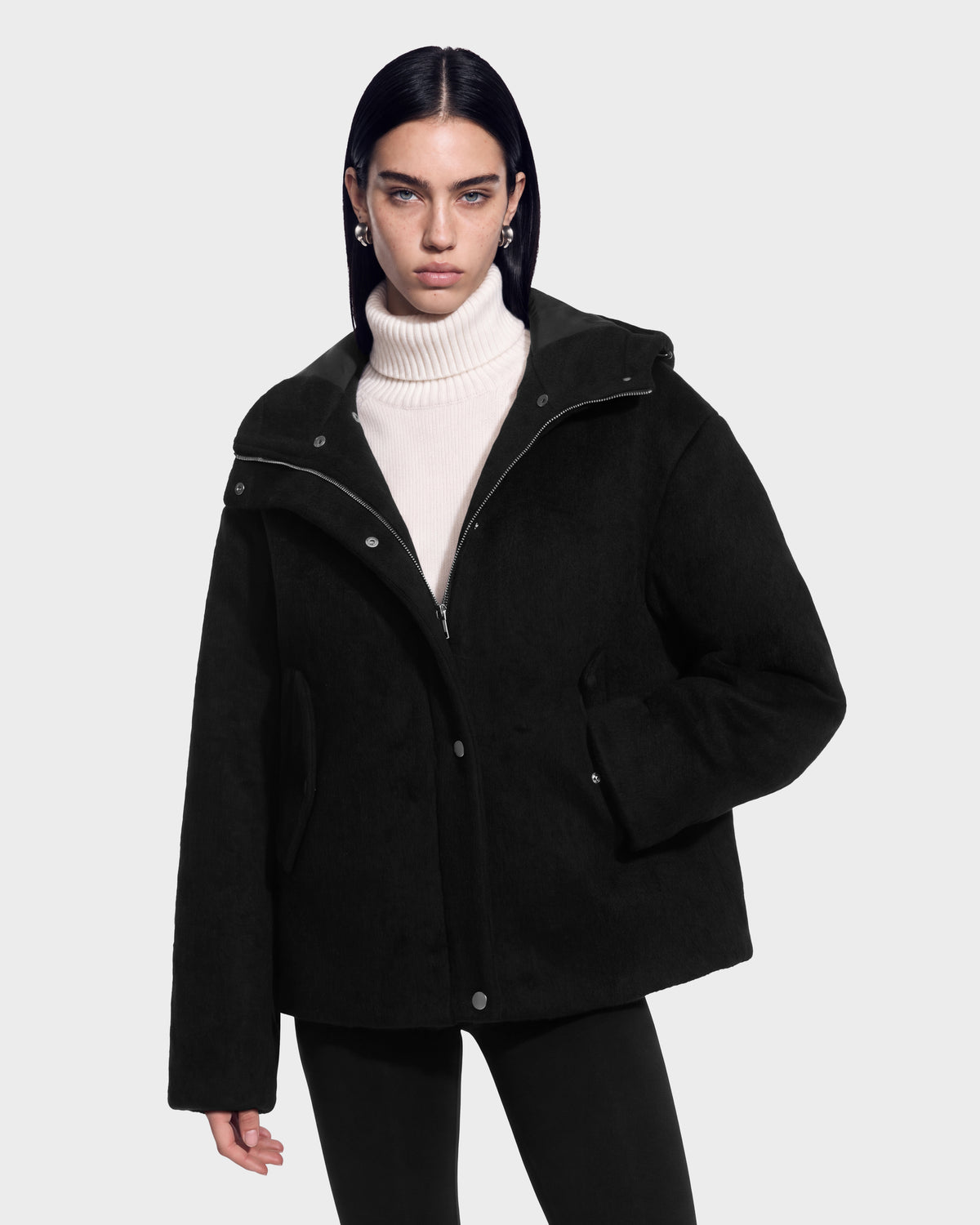 A person wears a black Rudsak HAZEL - 8126981 Black faux-fur trim hooded jacket over a cream-colored turtleneck sweater.
