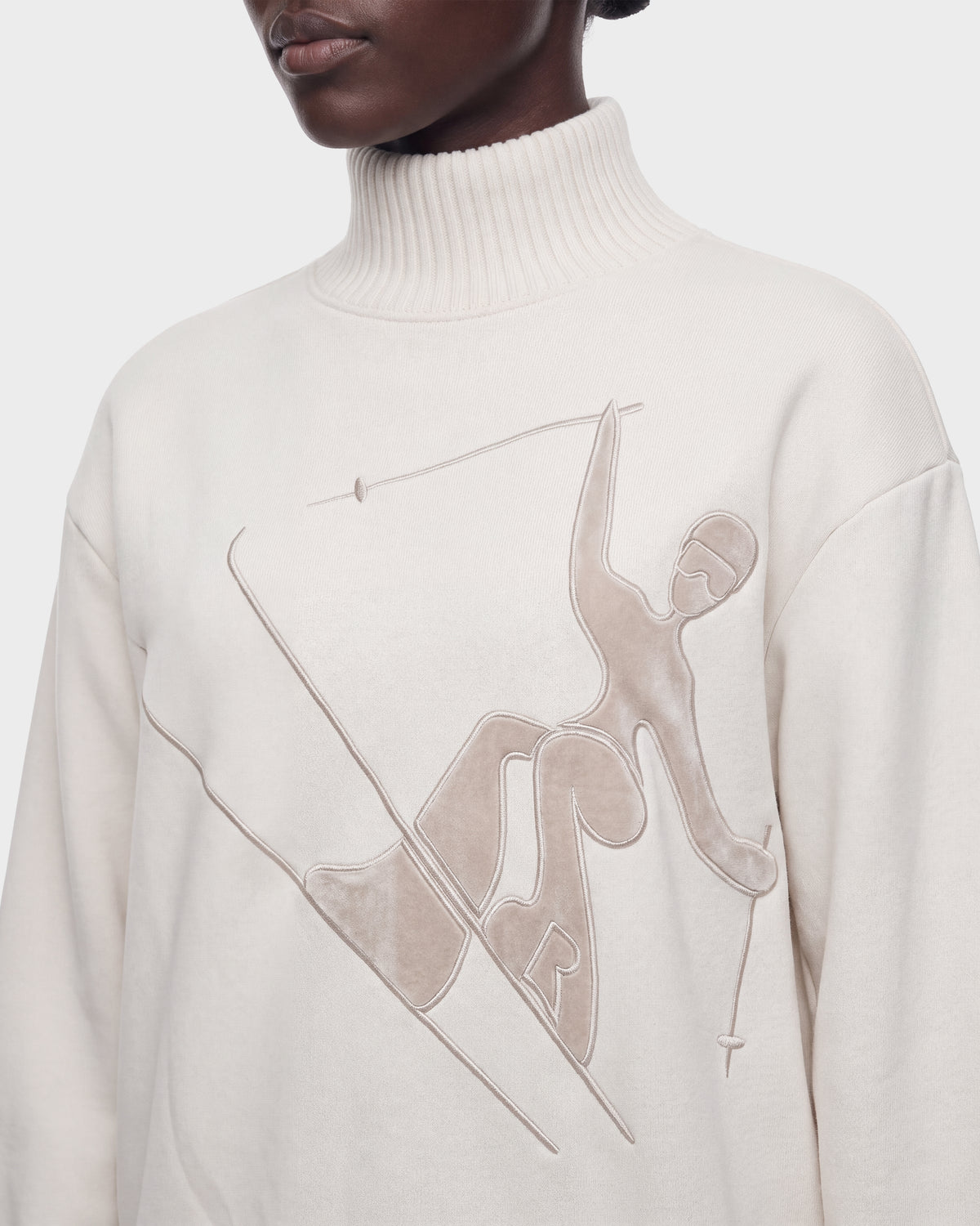 A person is shown wearing the Rudsak JOYCE E - 8526538 Vanilla turtleneck sweater, featuring an embossed abstract skier design on the front. Only their lower face, neck, and upper torso are visible against a plain background.