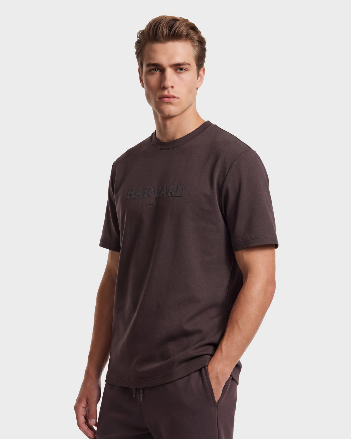 A young man wearing the Rudsak KARTER R HV - H525507 Espresso limited edition T-shirt and matching pants stands with one hand in his pocket, looking straight at the camera against a plain white background.