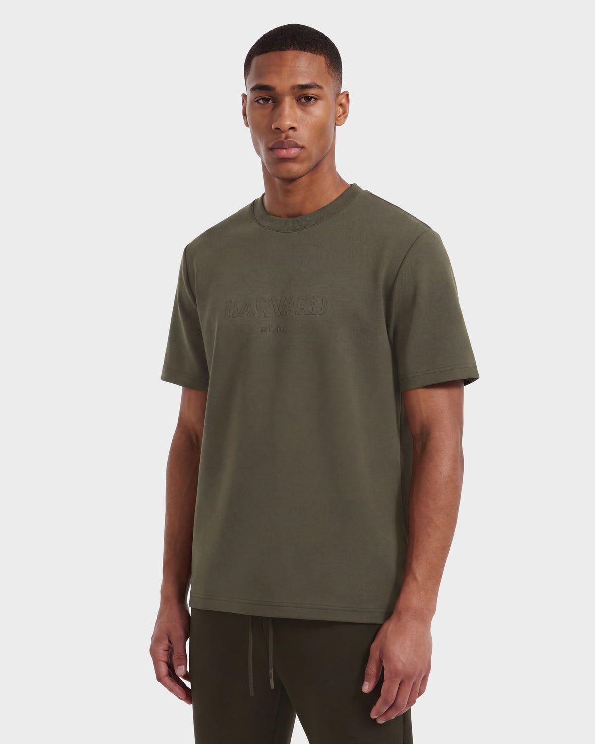 A man wearing the KARTER R HV - H525507 Olive T-shirt and matching pants from Rudsak stands against a plain white background, looking at the camera with a neutral expression, effortlessly capturing the essence of contemporary streetwear.