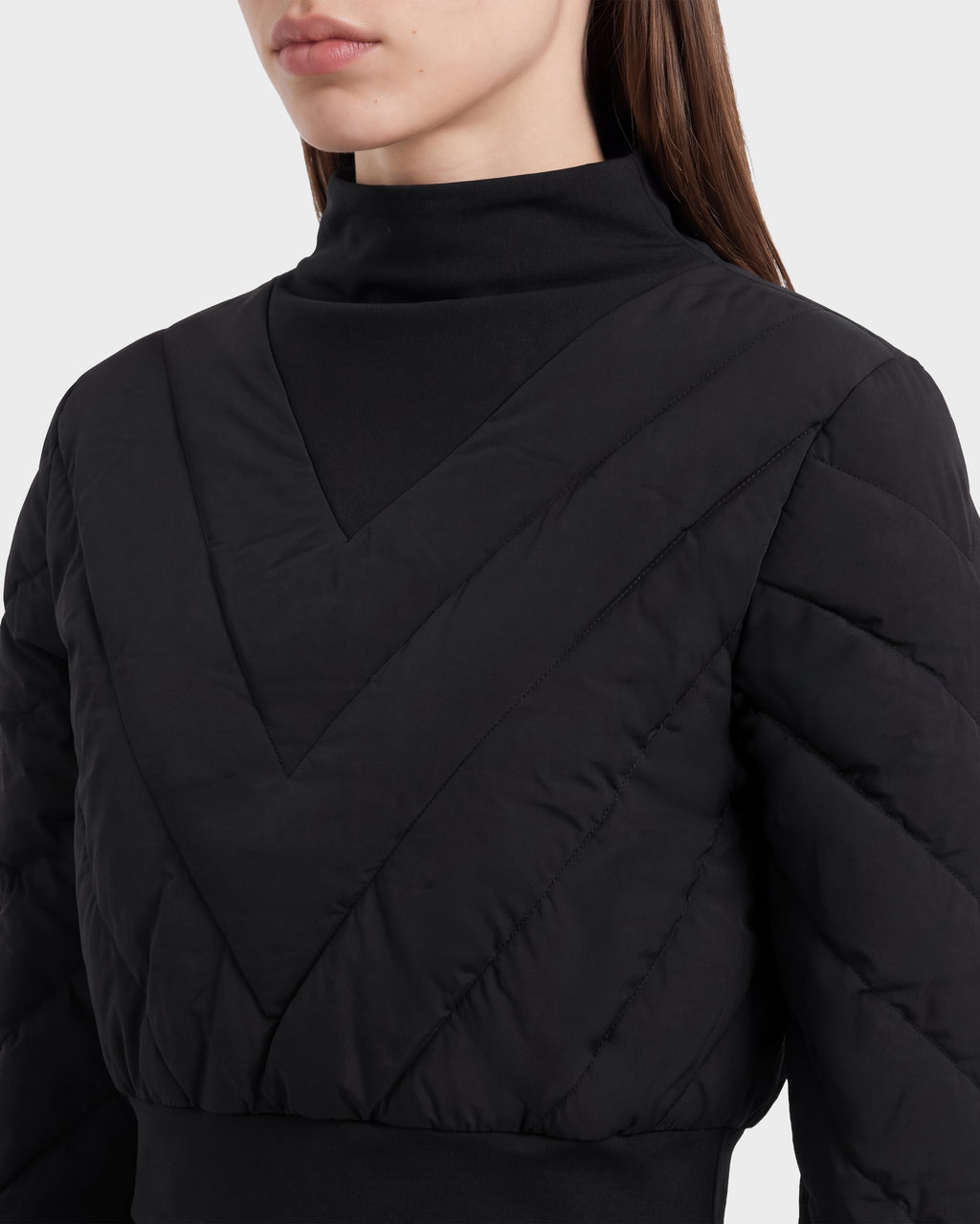 A woman shown from the shoulders up wears the Rudsak KATYA - 8526531 Black jacket, featuring a black quilted, V-patterned design with down insulation and a high-neck black inner layer that evokes après-ski style.