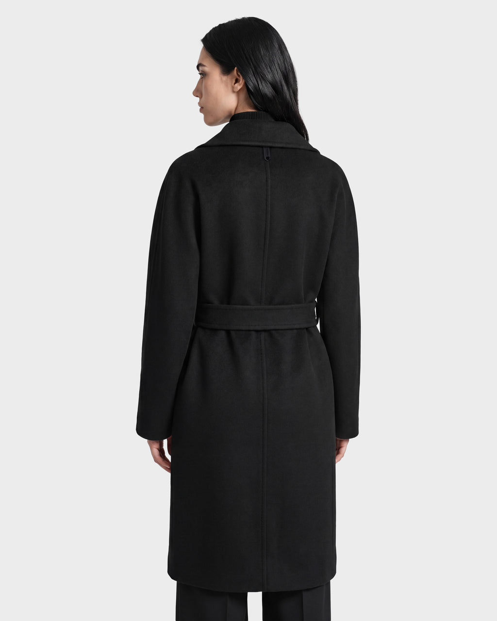 A woman with long dark hair, seen from behind, wears the Rudsak KOURT W - 8124702 Black belted wool coat, standing against a plain light gray background.