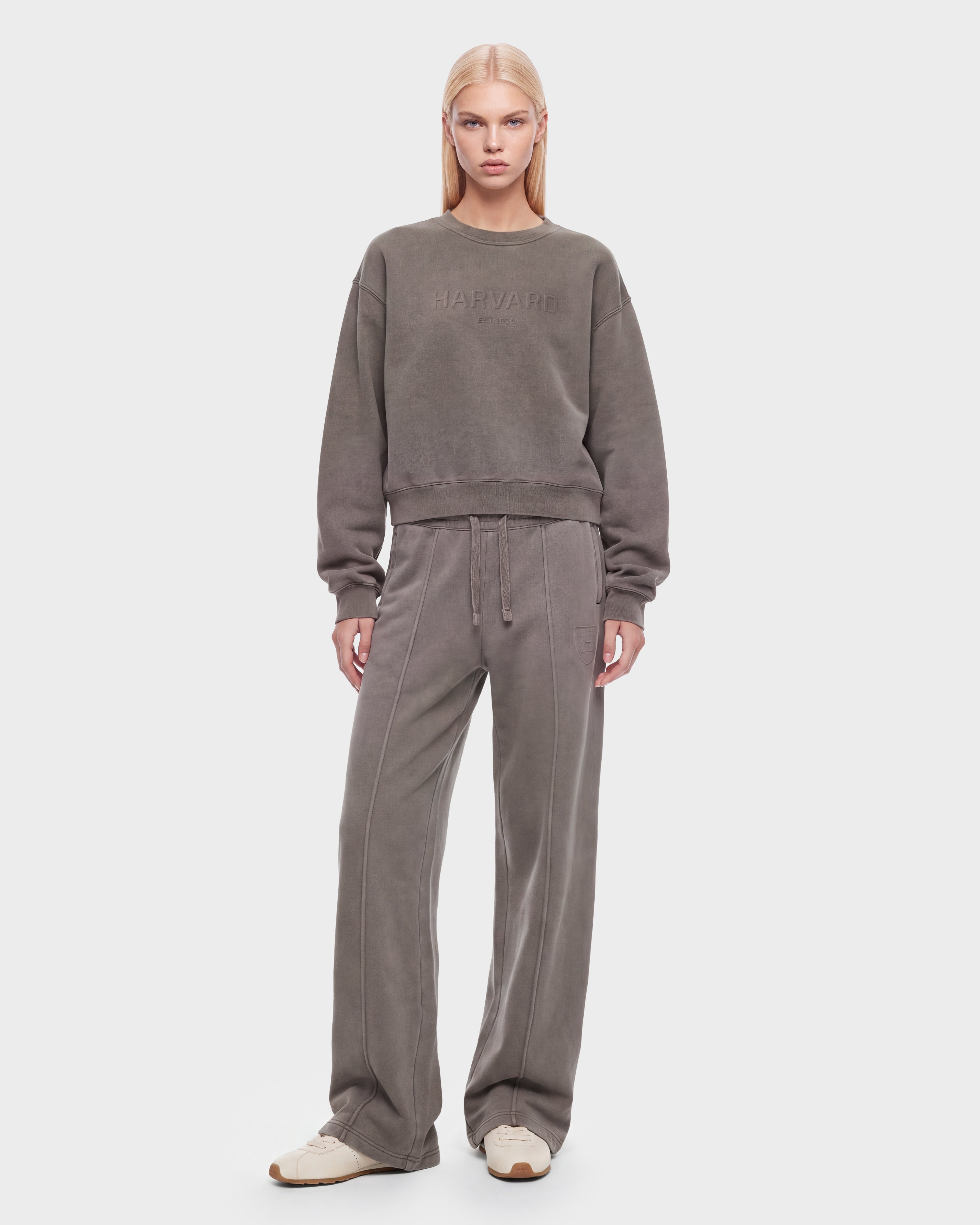 A person wearing the Rudsak LEXYE HV - H526900 Taupe sweat set, featuring a loose-fitting taupe sweatshirt and matching wide-leg sweatpants, paired with white sneakers and standing against a plain white background.