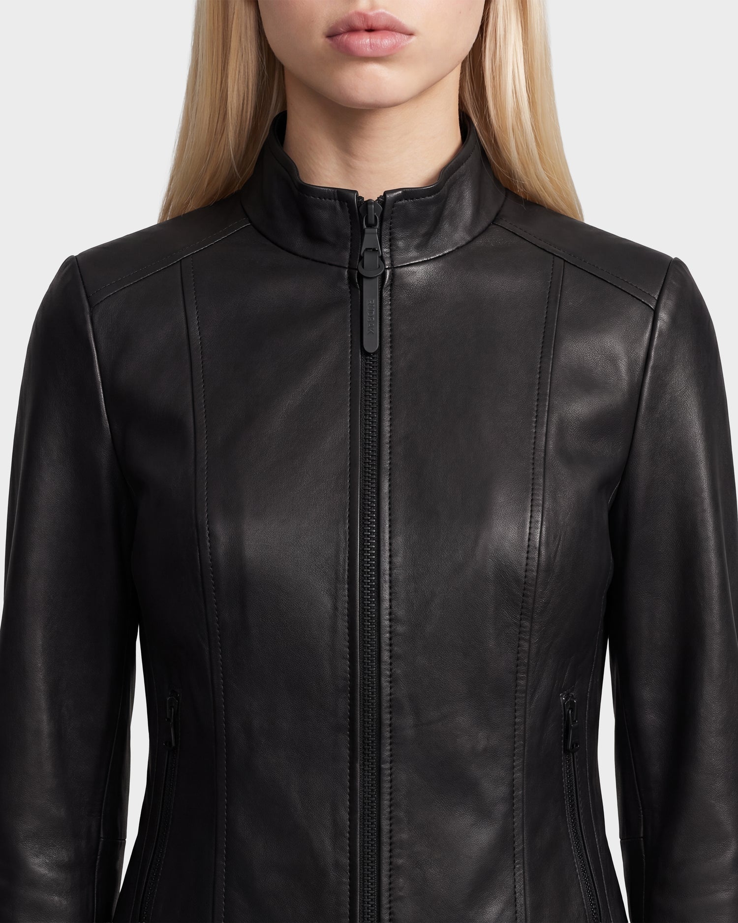 A woman wearing the Rudsak MARIAH - L124511 Black moto biker jacket, featuring a fitted silhouette, front zipper, and standing collar, shown from the shoulders to just above the waist.